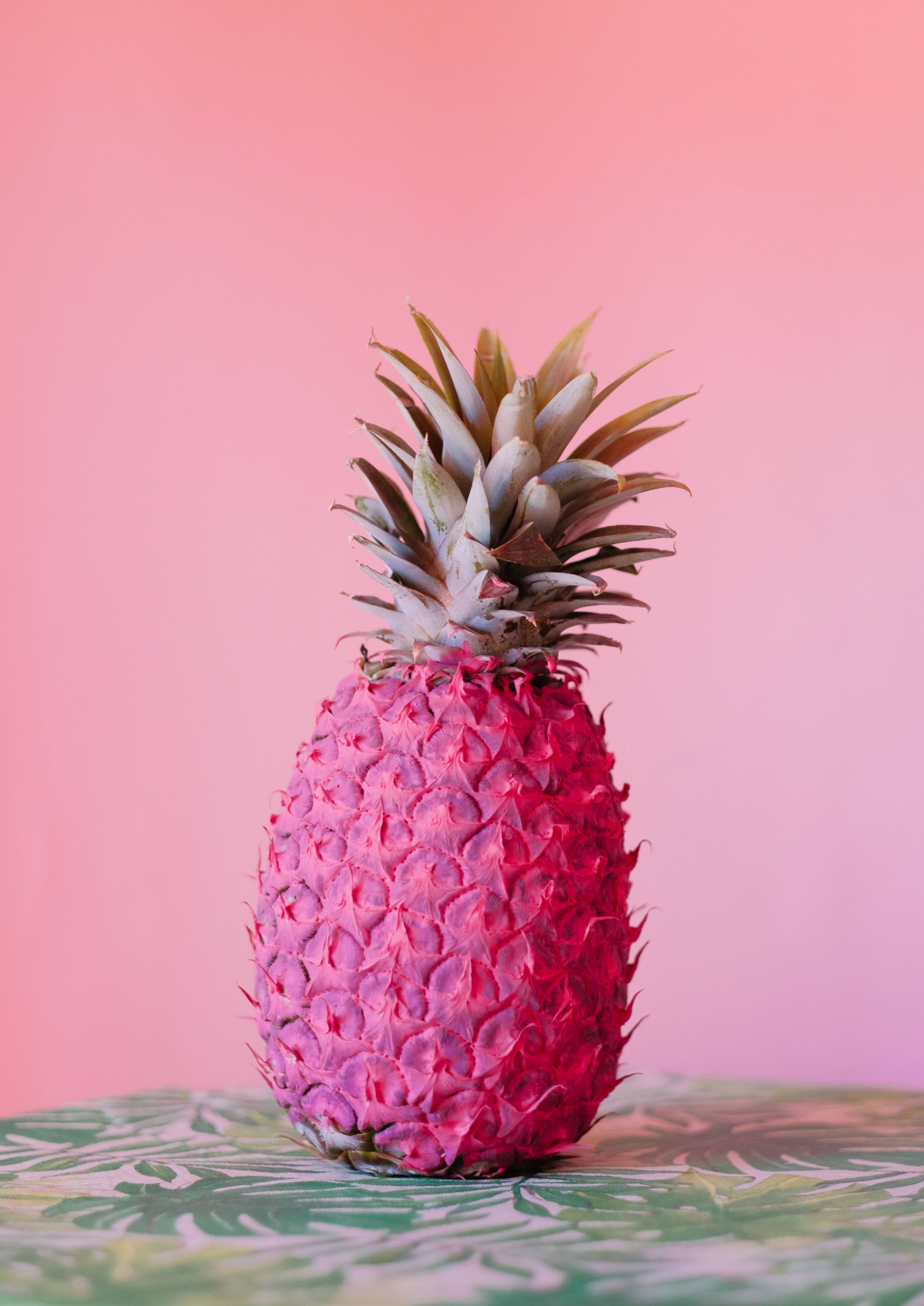 bright pink pineapple, green crown, tropical leaf patterned surface, 4K Phone Wallpaper