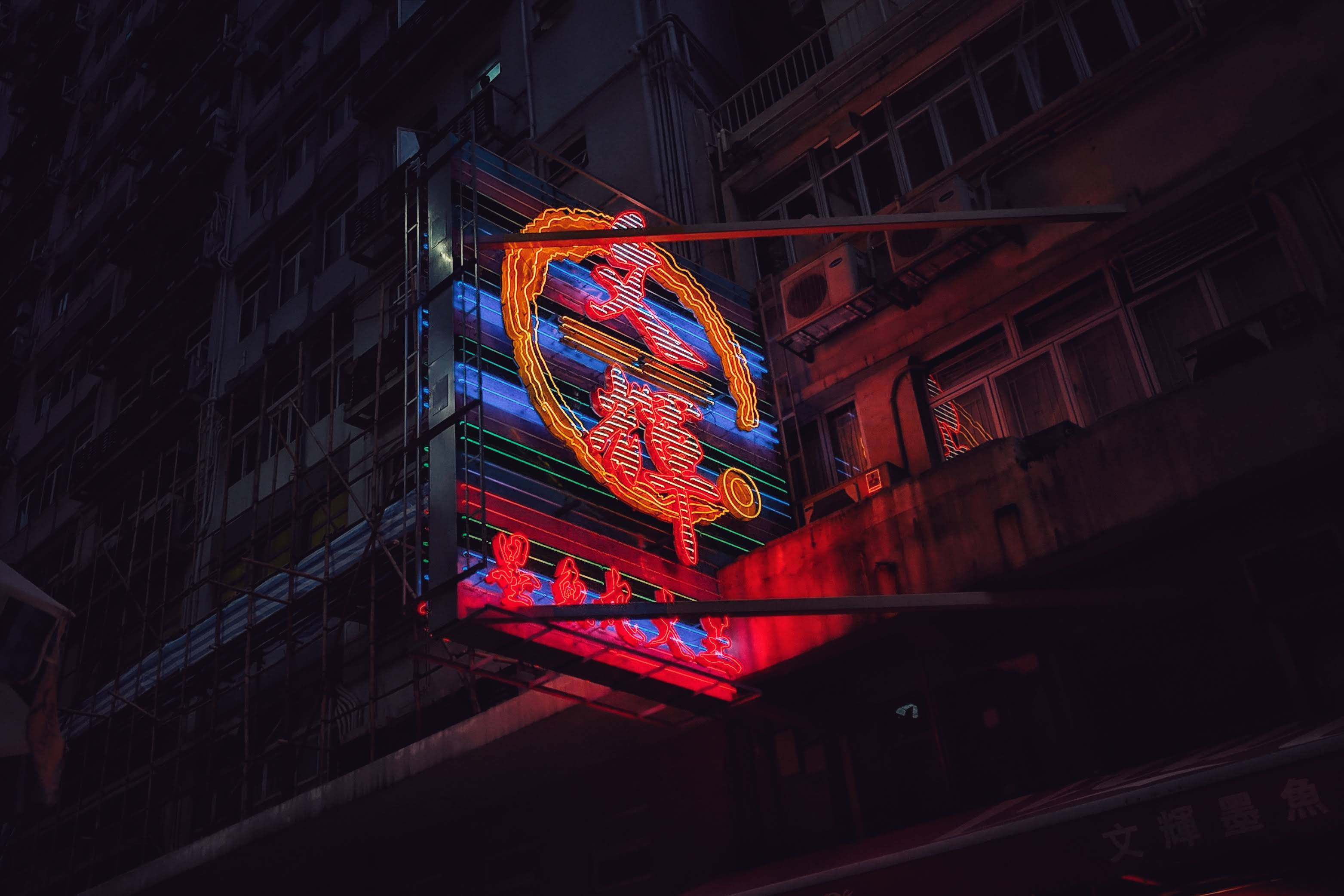 neon sign, red and blue glowing characters, dark urban building facade, 2K Desktop Wallpaper