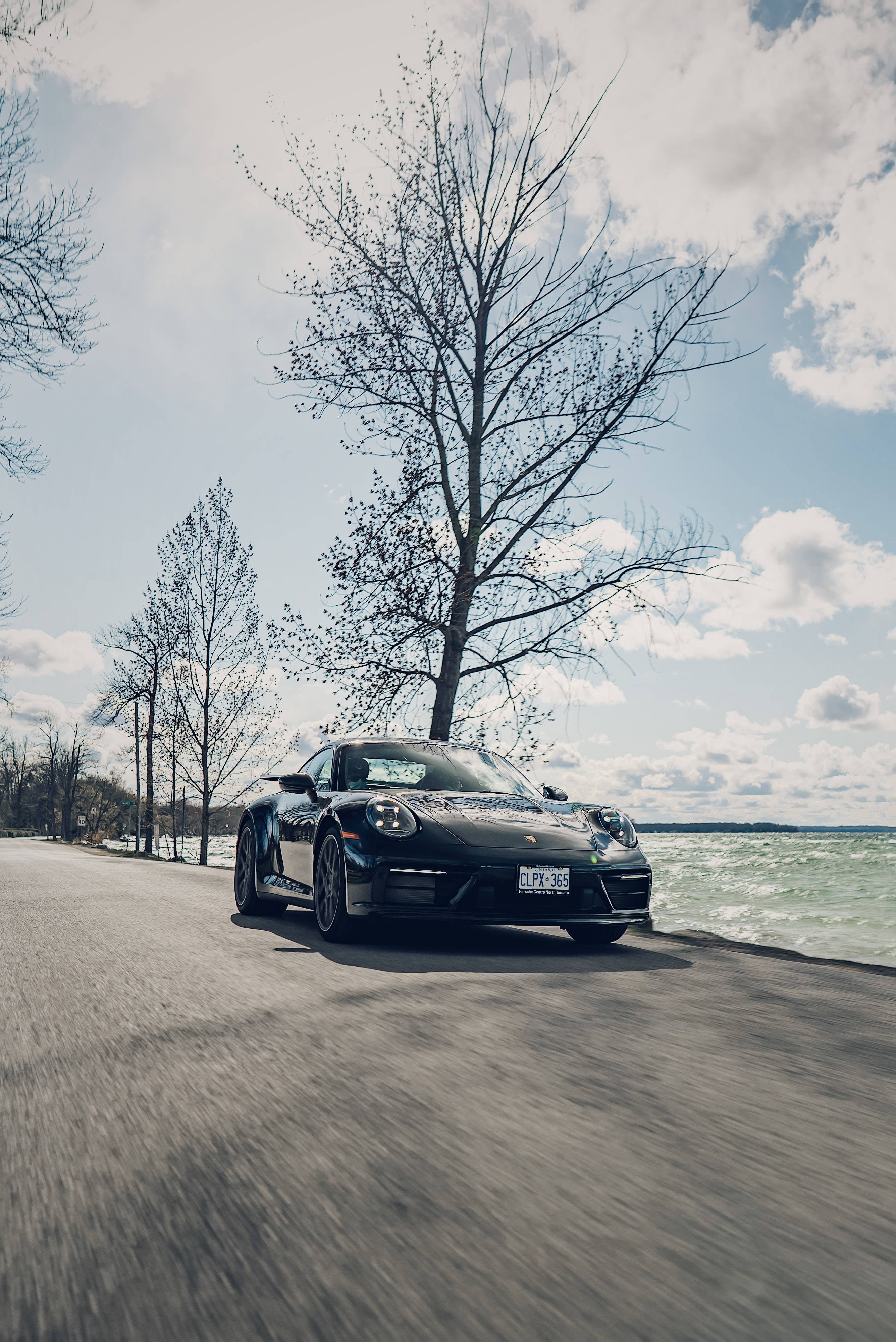 Black Porsche, coastal road, bare trees, 4K Phone Wallpaper