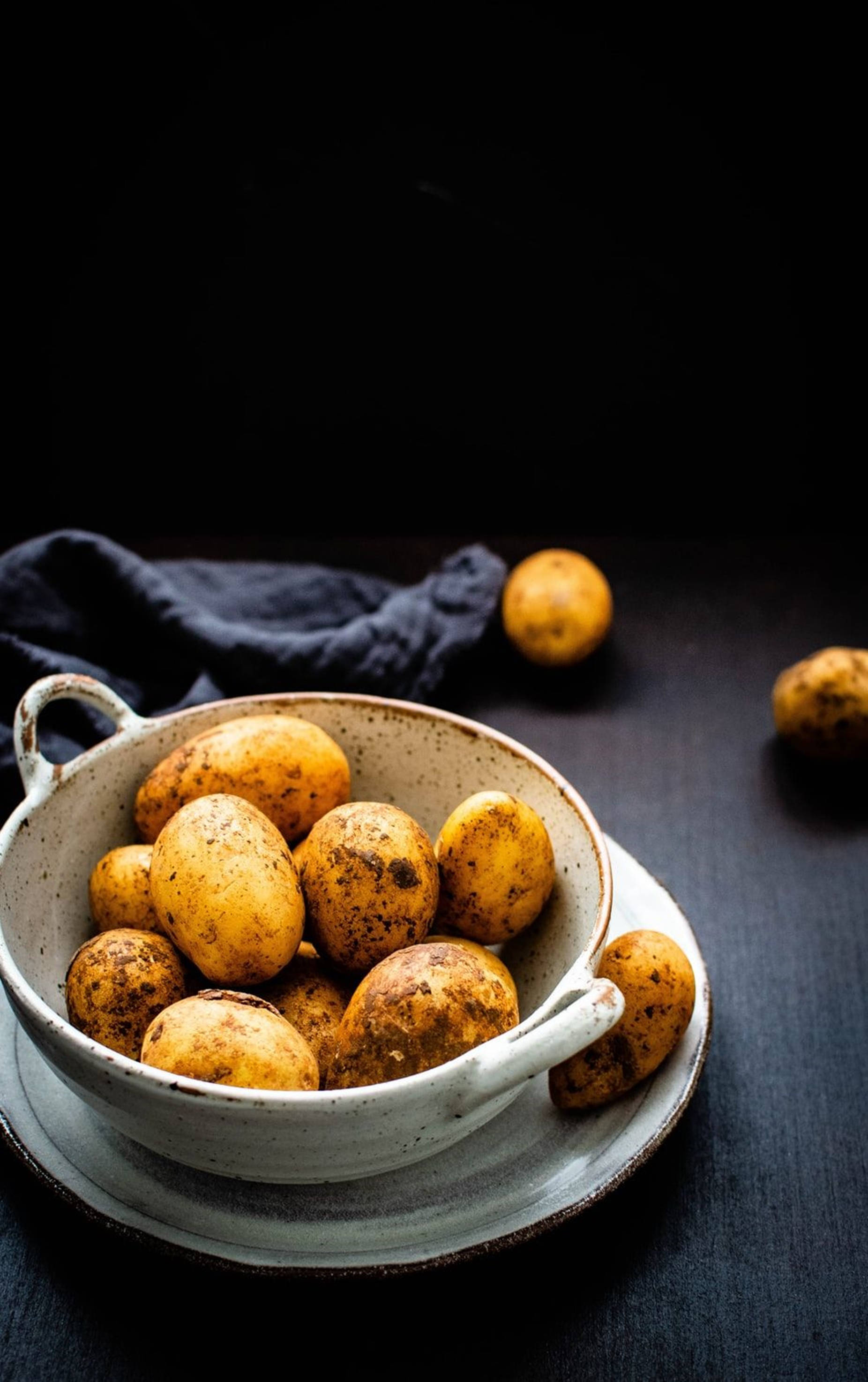white ceramic bowl, earthy yellow potatoes, dark wooden surface, 2K Phone Wallpaper