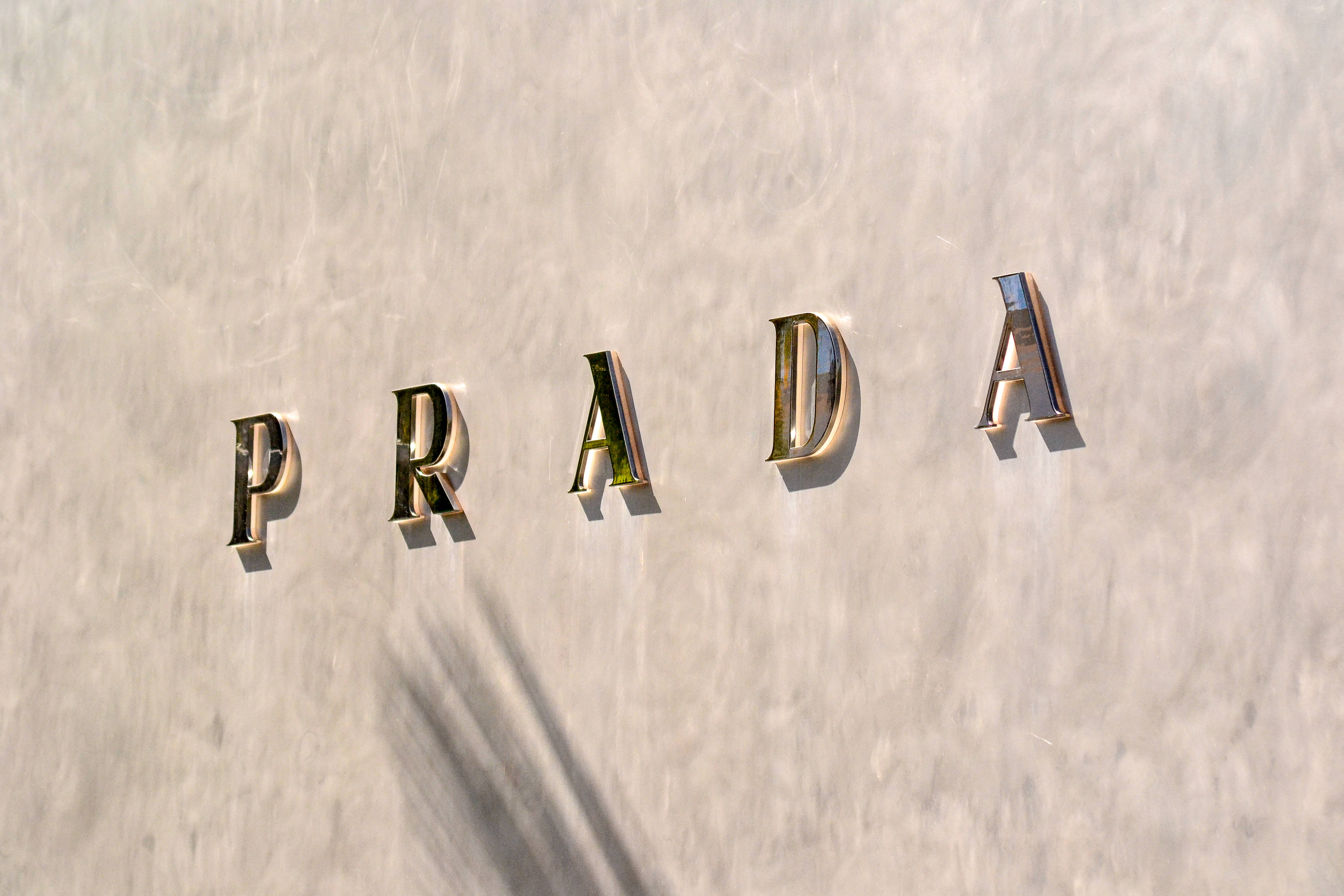 Prada, gold letters, textured off-white wall, 4K Desktop Wallpaper