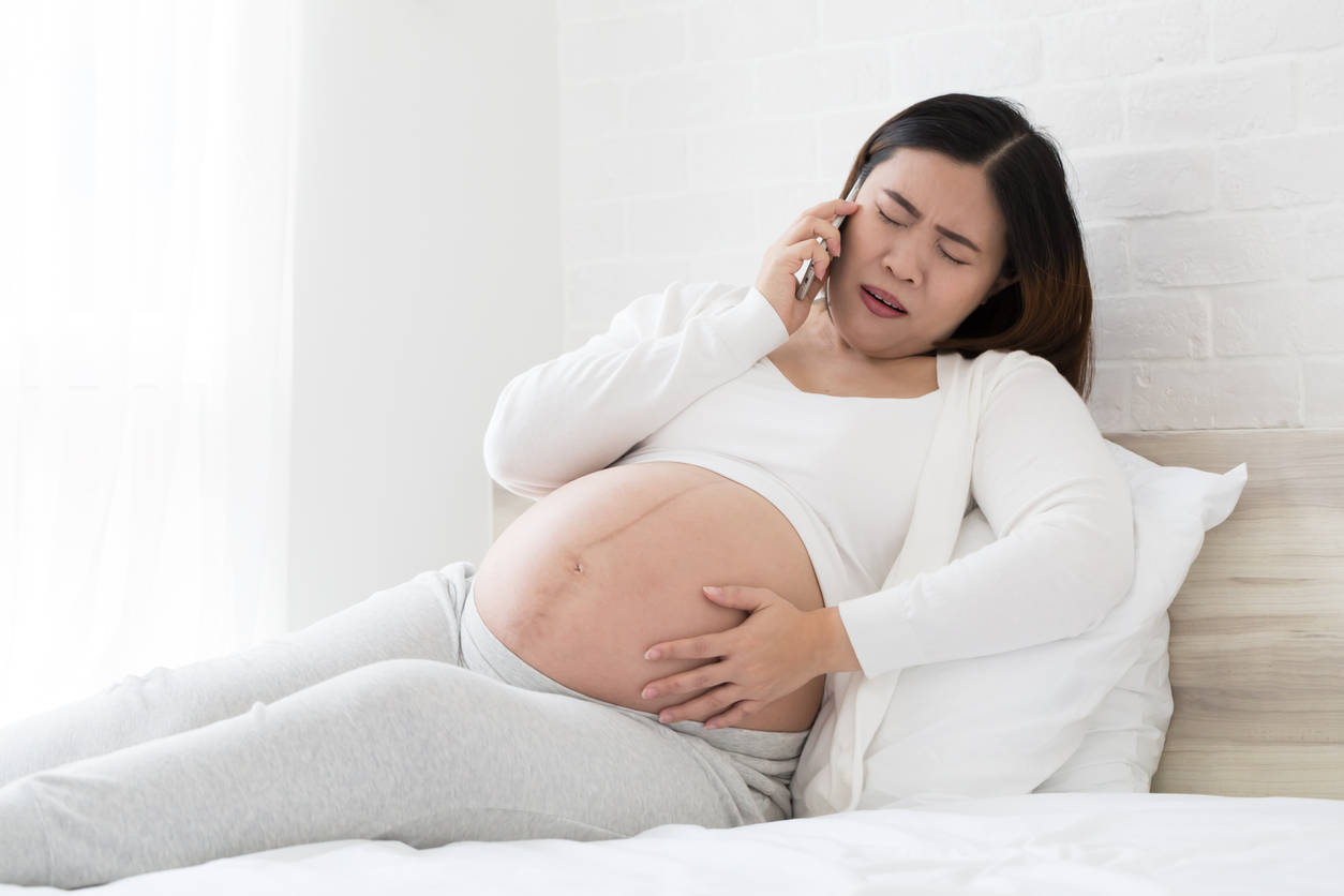 pregnant woman, white lounges on a bed, holding her belly, SD Desktop Wallpaper
