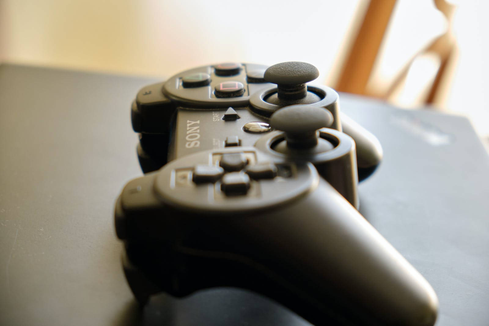 black Sony PlayStation 3 controller, dark surface, soft warm lighting, HD Desktop Wallpaper