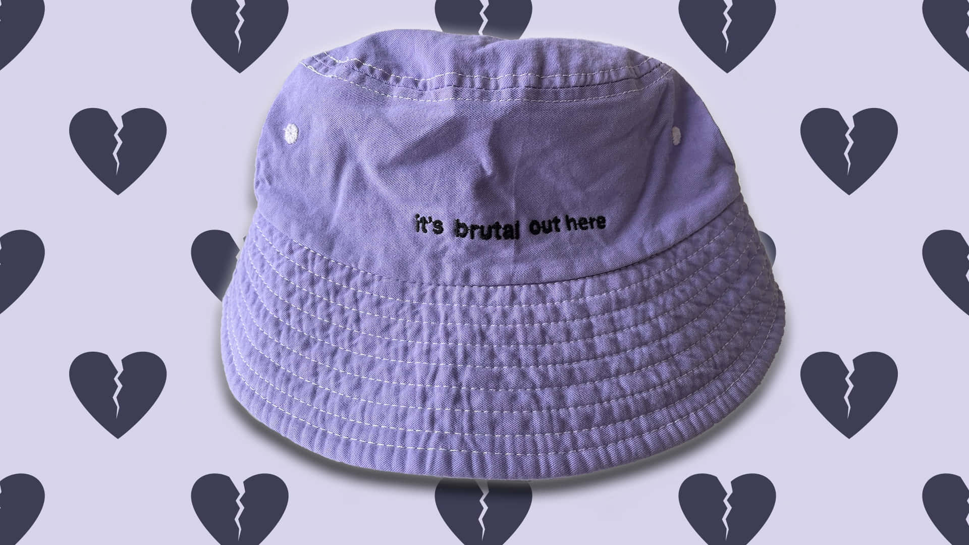 lavender bucket hat, black text reading it's brutal out here, light purple background, Full HD Desktop Wallpaper
