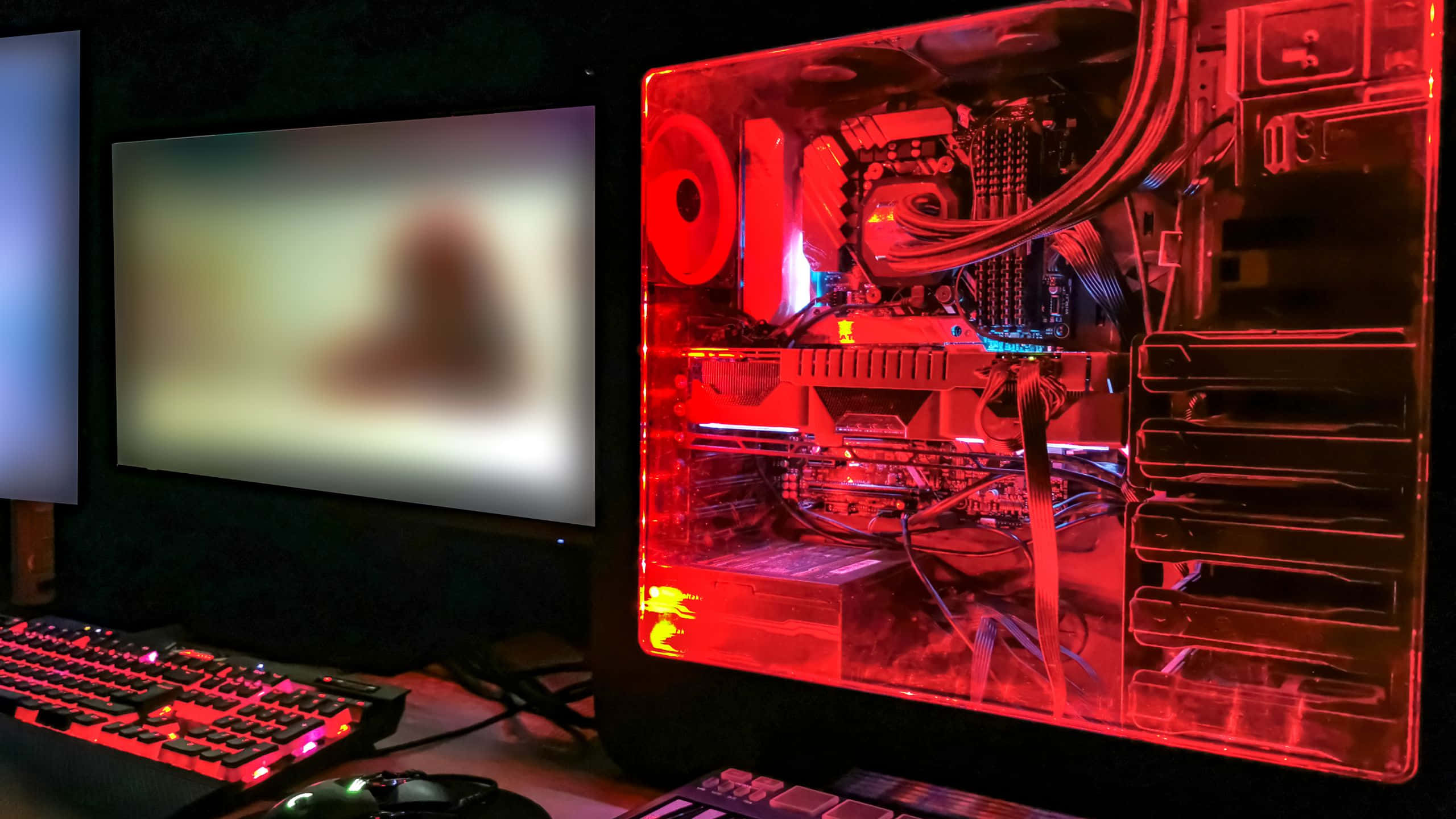 Red PC, glowing red transparent gaming PC case, blurred monitor, 2K Desktop Wallpaper