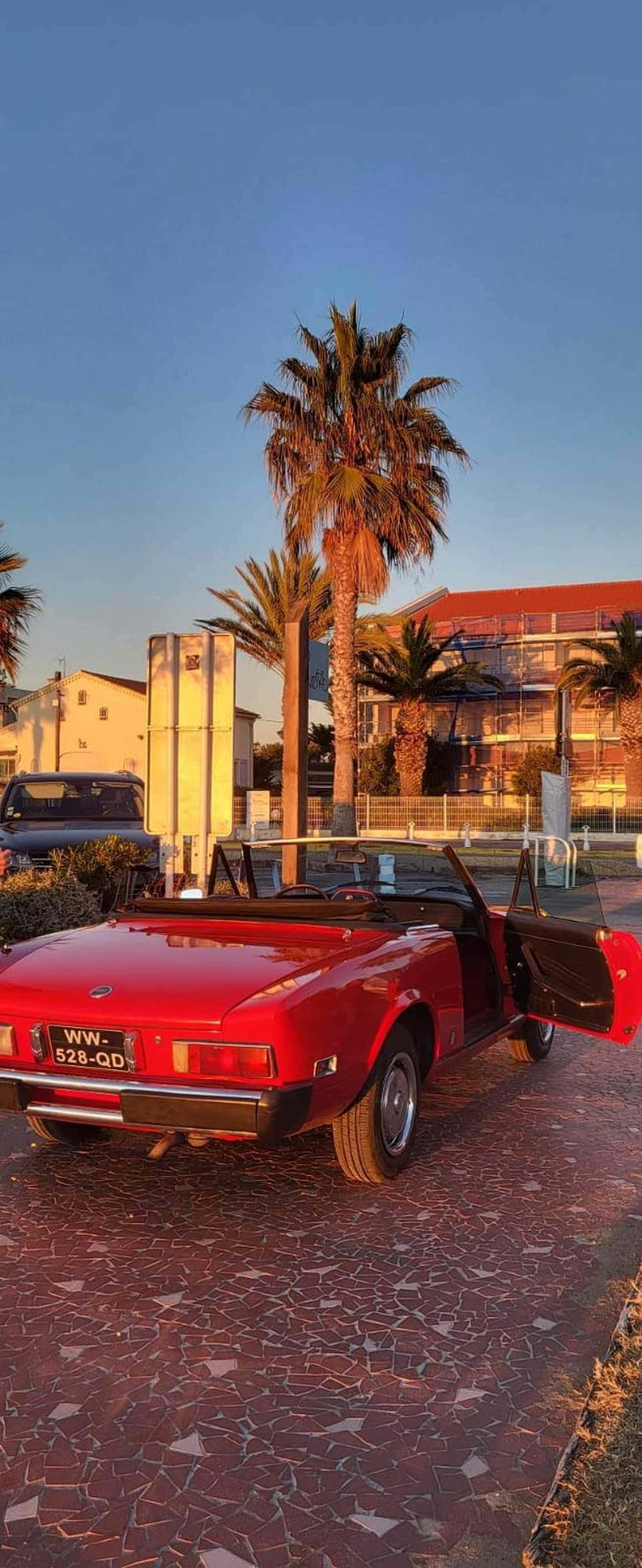 vibrant red classic convertible, mosaic-tiled street, clear blue sky, 4K Phone Wallpaper