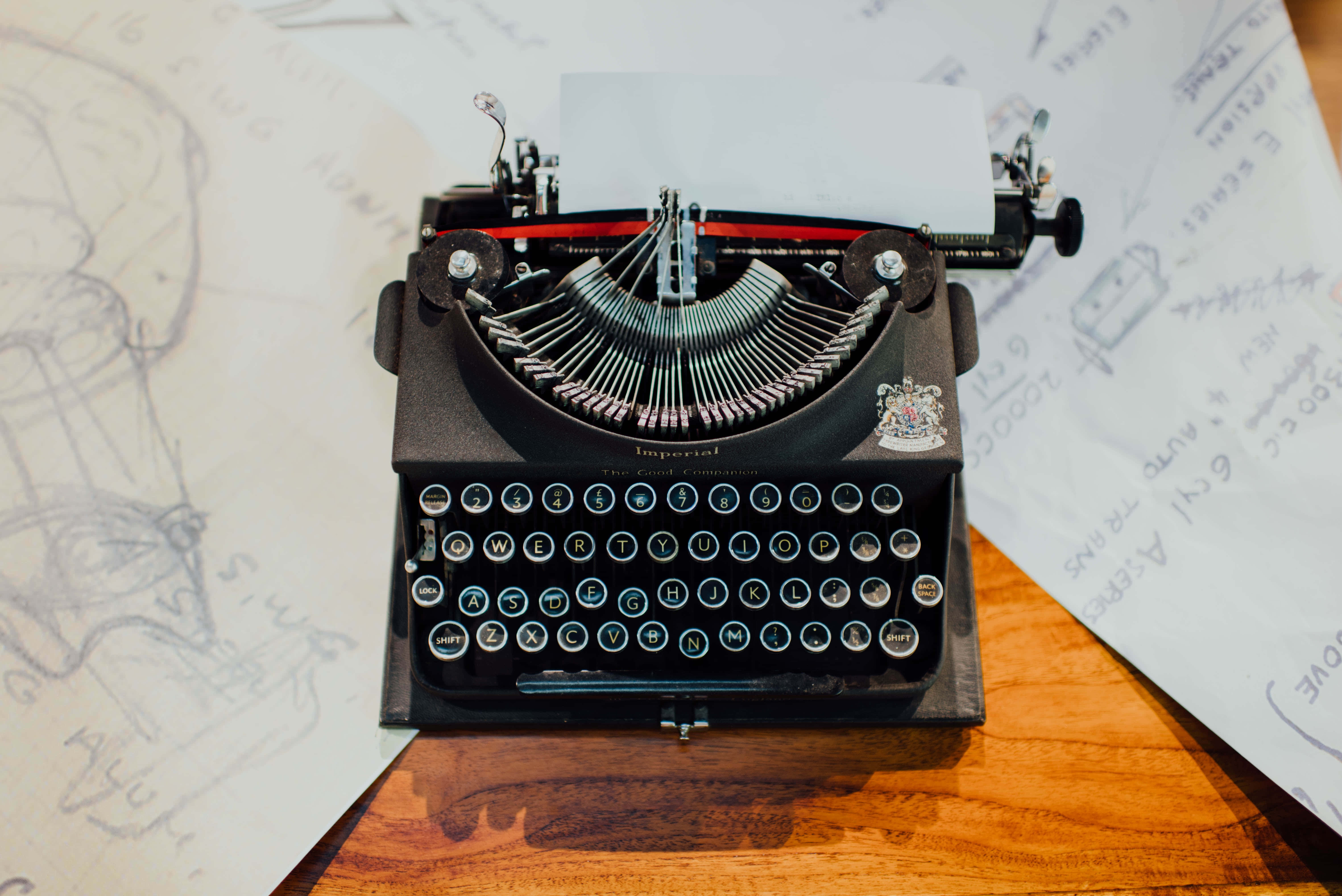 vintage black typewriter, wooden desk, scattered handwritten sketches, 5K Desktop Wallpaper