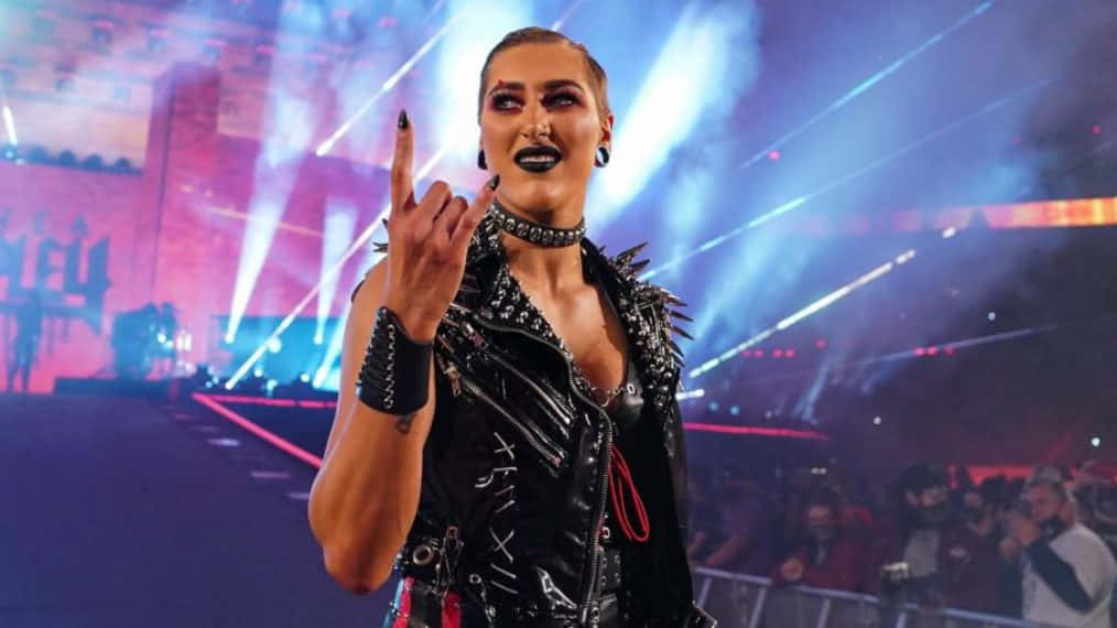 Rhea Ripley, spiked black leather outfit, rock hand gesture, SD Desktop Wallpaper