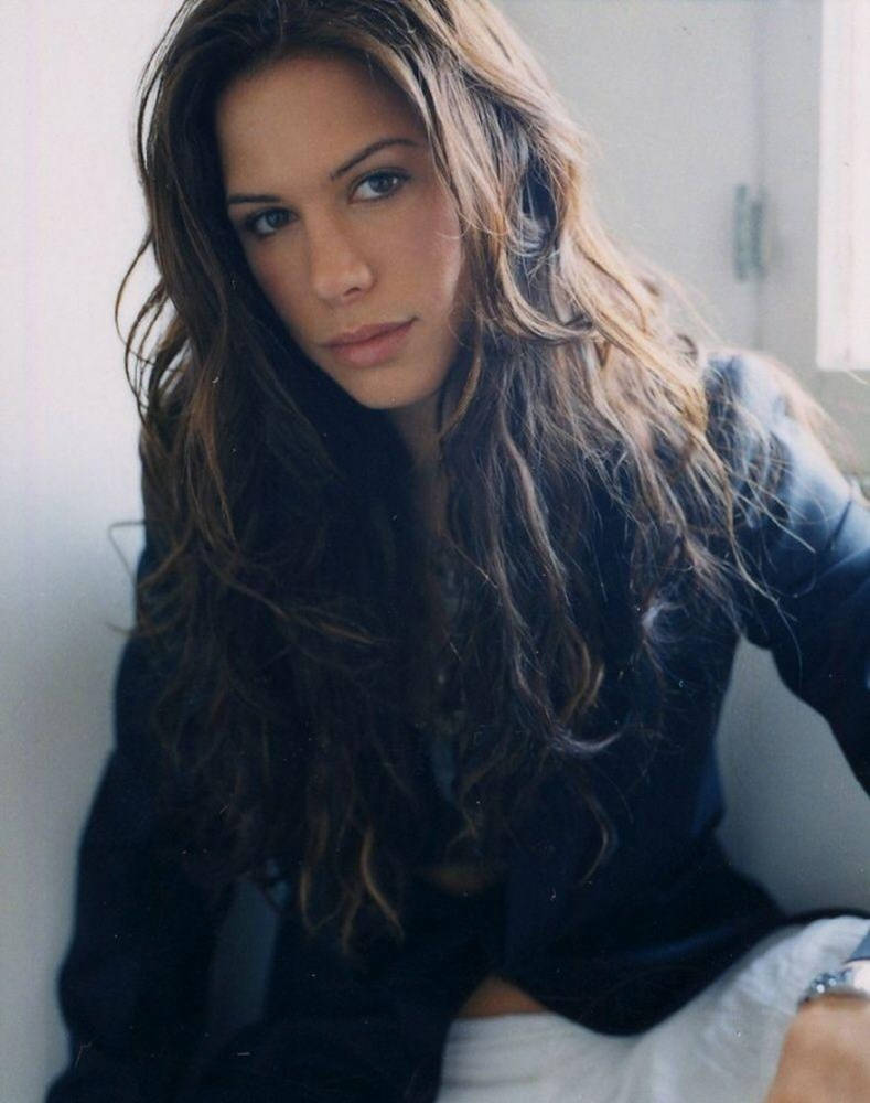 Rhona Mitra, long wavy brown hair, softly lit indoor space, SD Phone Wallpaper