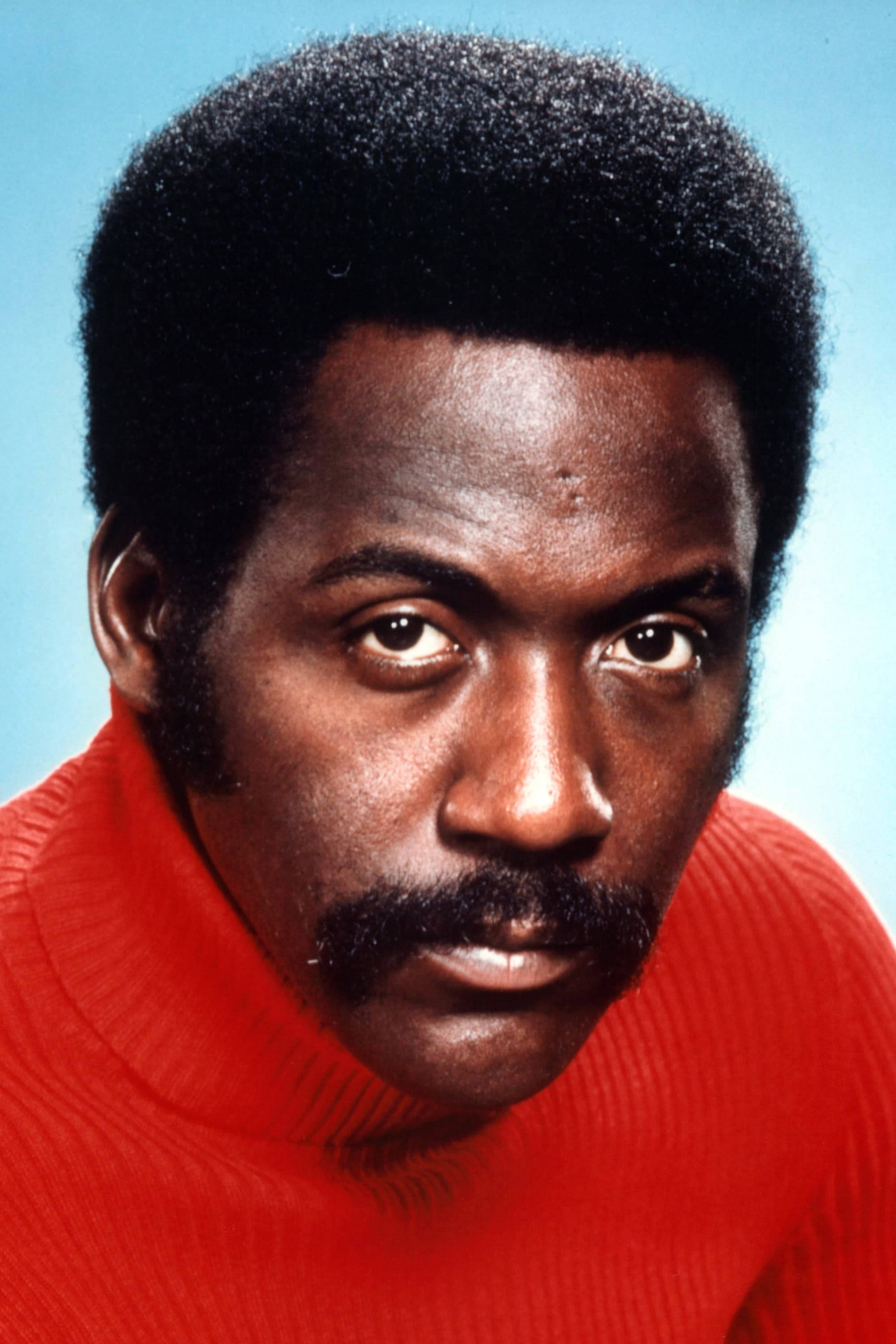 Richard Roundtree, red turtleneck, solid blue background, 2K Phone Wallpaper