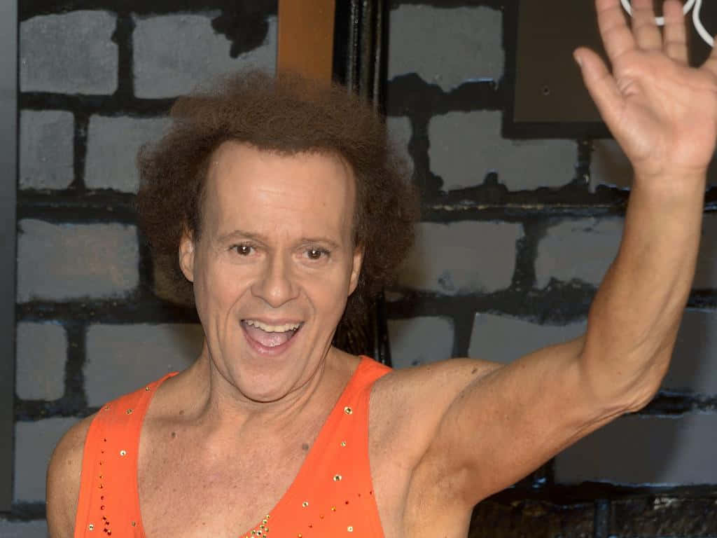Richard Simmons, bright orange sequined top, gray brick wall, SD Desktop Wallpaper