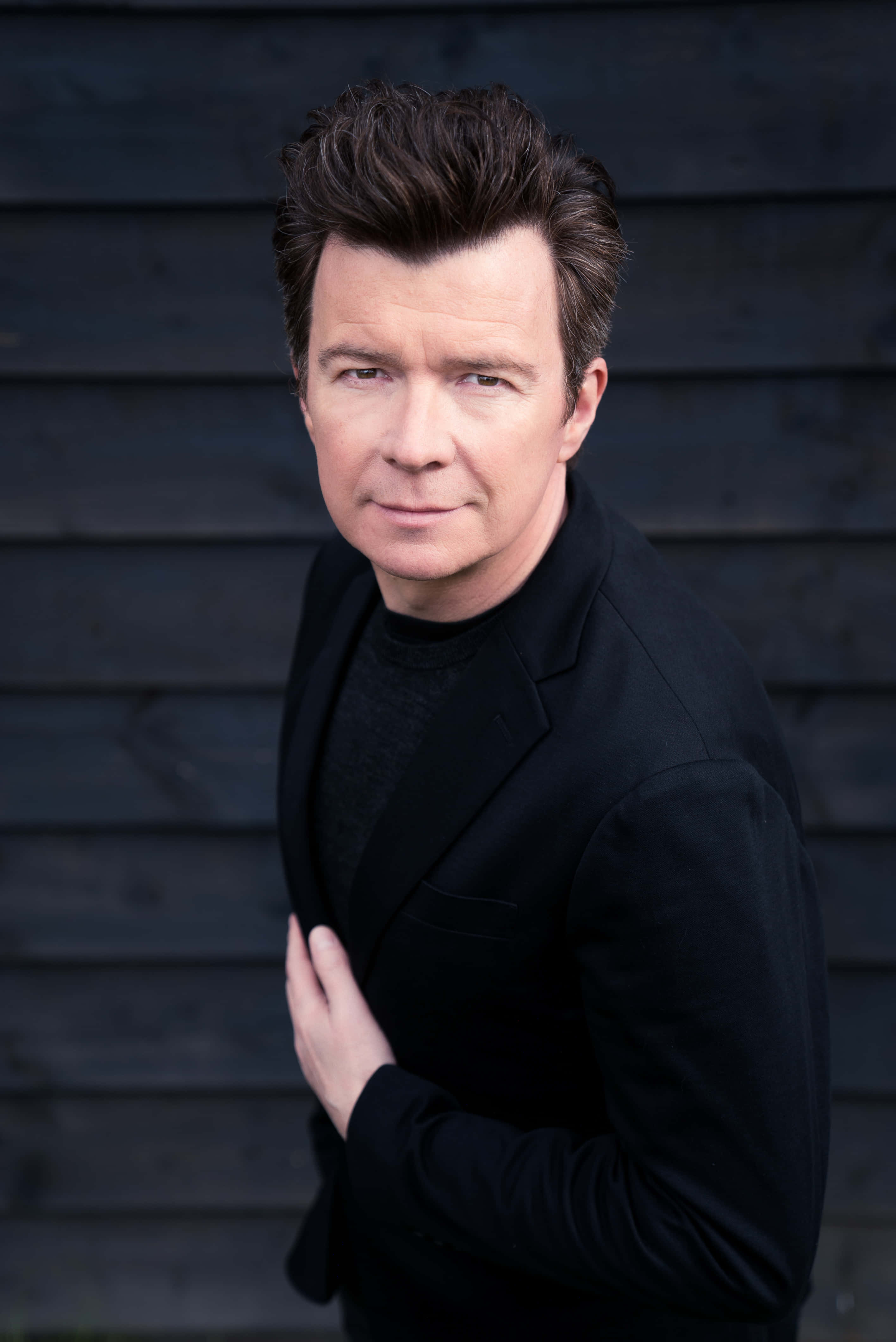 Rick Astley, black blazer, dark wooden wall, 4K Phone Wallpaper