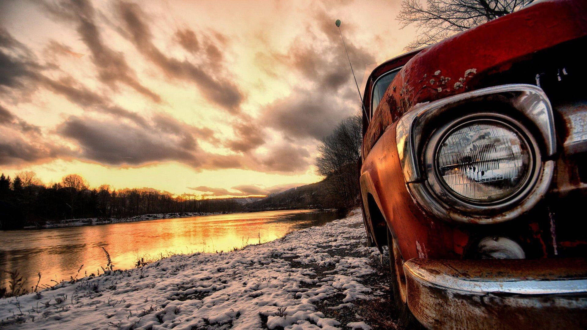 rusty red vintage car, snow-dusted riverbank, dramatic sunset sky, Full HD Desktop Wallpaper