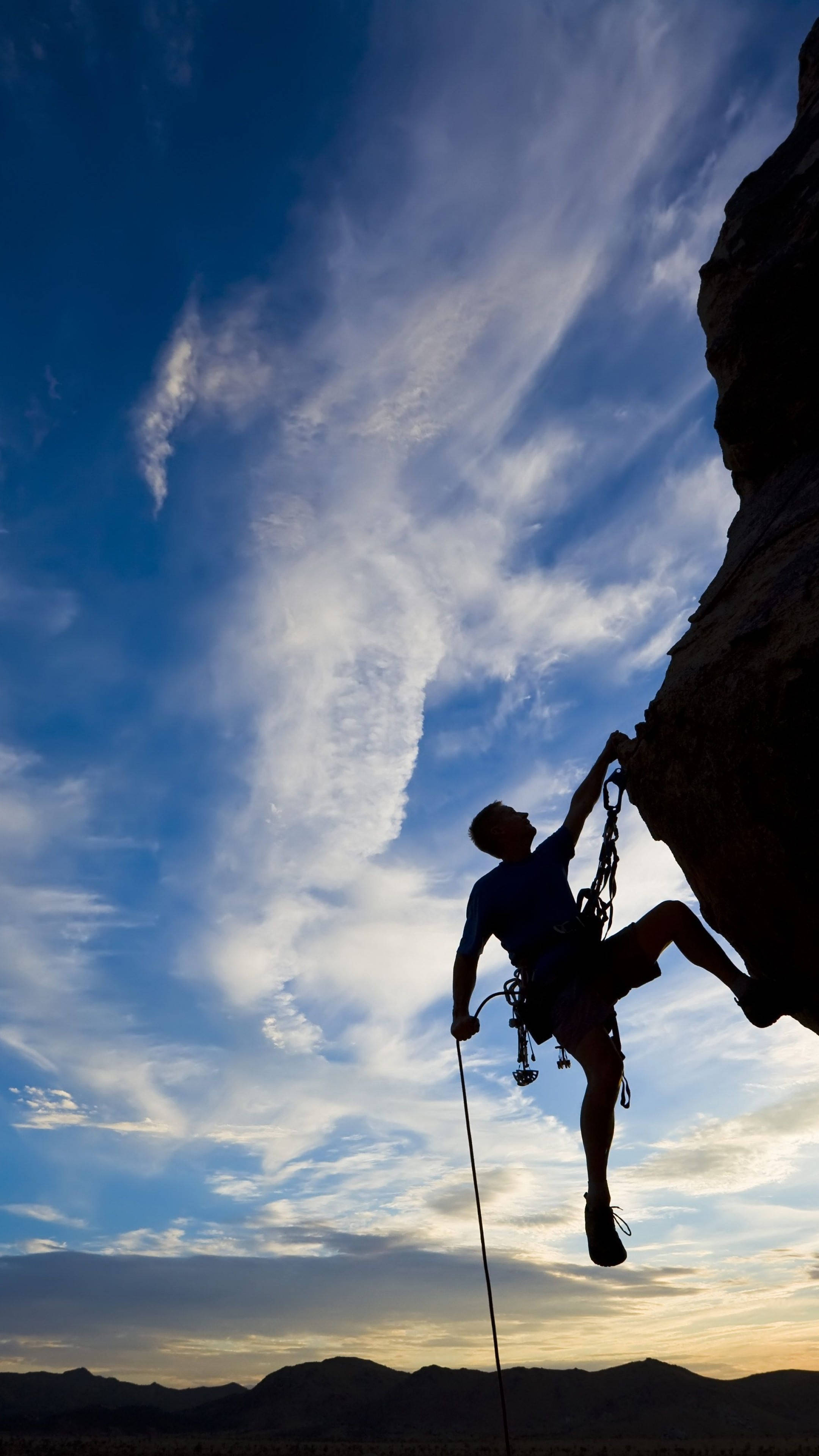 silhouetted man, rugged cliff, vibrant blue sky, 4K Phone Wallpaper