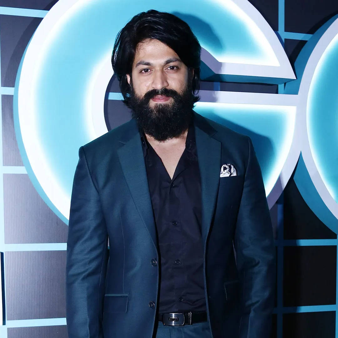 Rocking Star Yash, dark suit, glowing blue geometric backdrop, SD Desktop Wallpaper