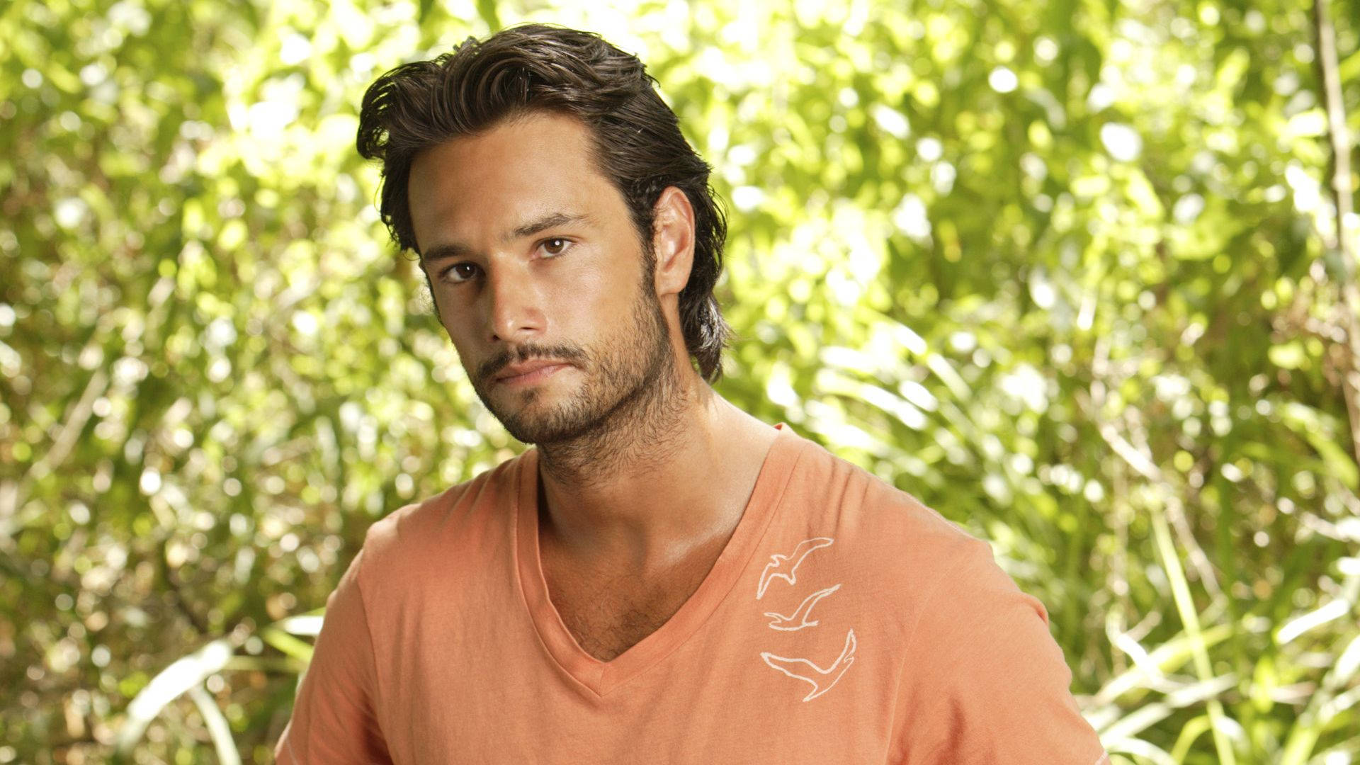 Rodrigo Santoro, orange v-neck shirt, bright green leafy background, Full HD Desktop Wallpaper