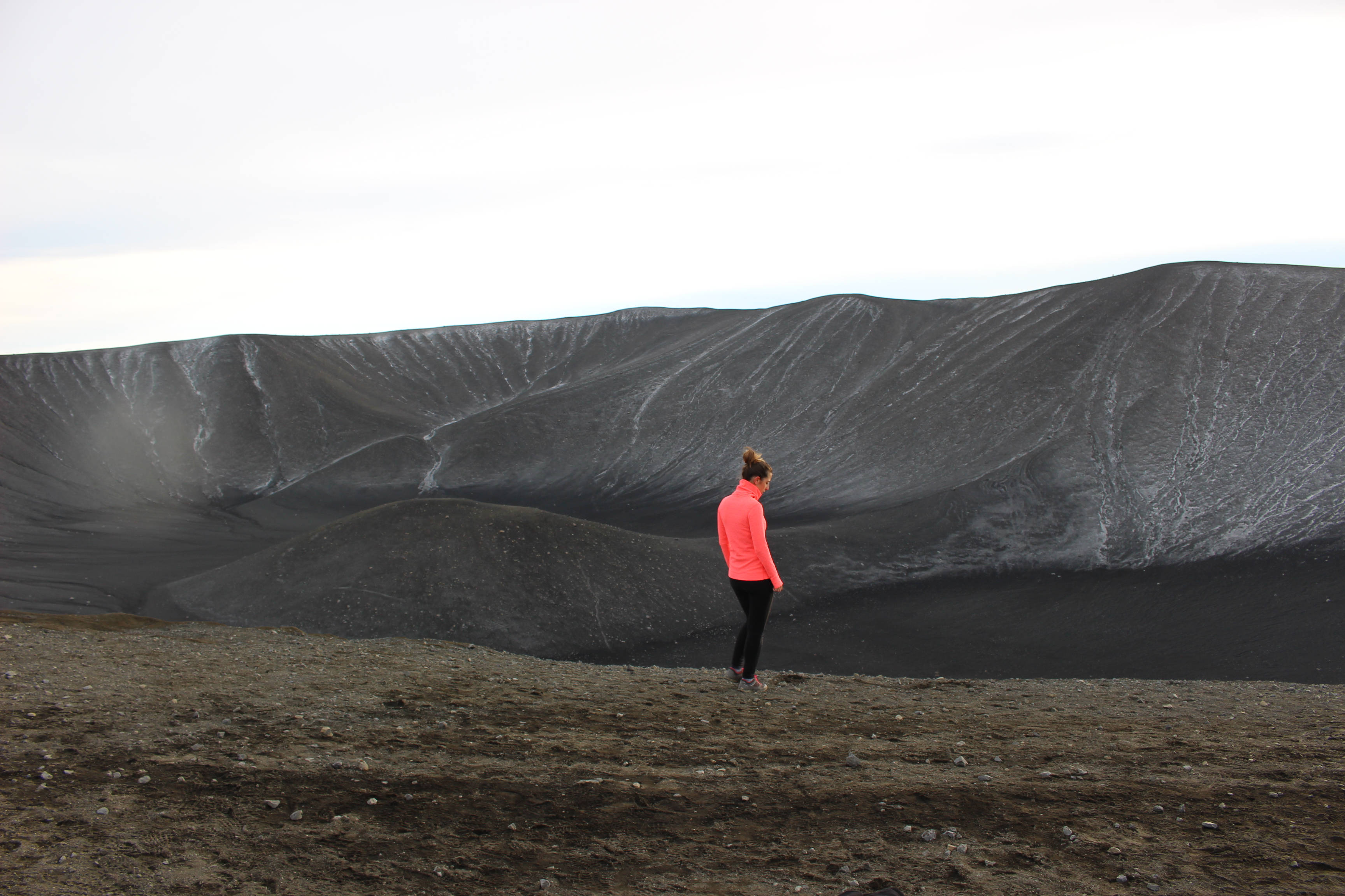 bright pink jacket, barren volcanic landscape, vast dark crater, 2K Desktop Wallpaper