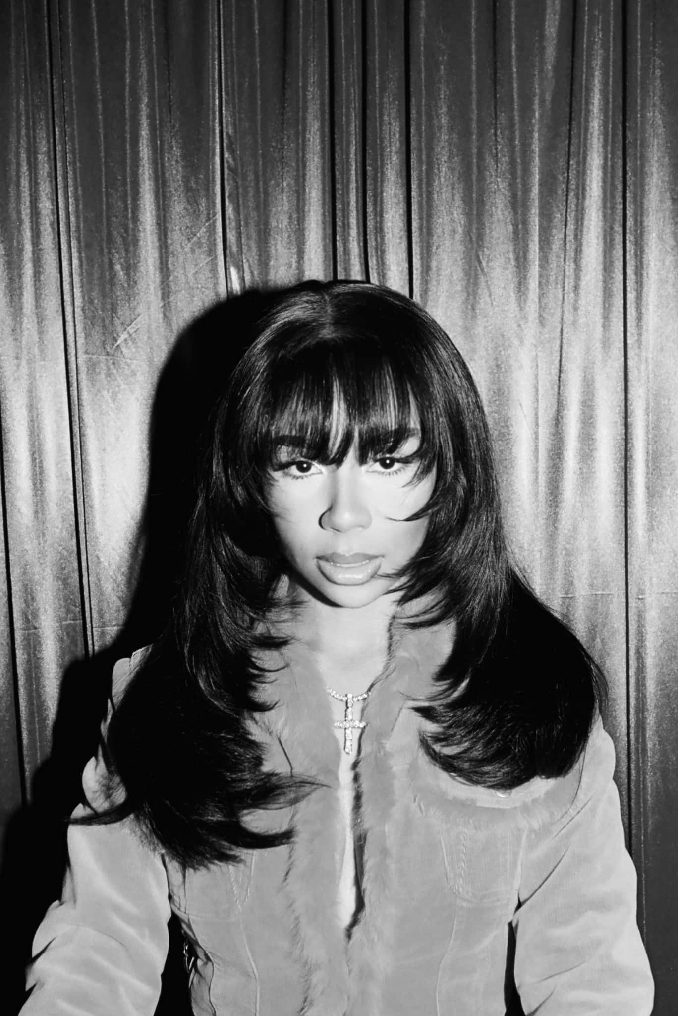 A striking black and white portrait of a woman with long hair and bangs wearing a fur-trimmed jacket against a draped curtain backdrop., Full HD Phone Wallpaper