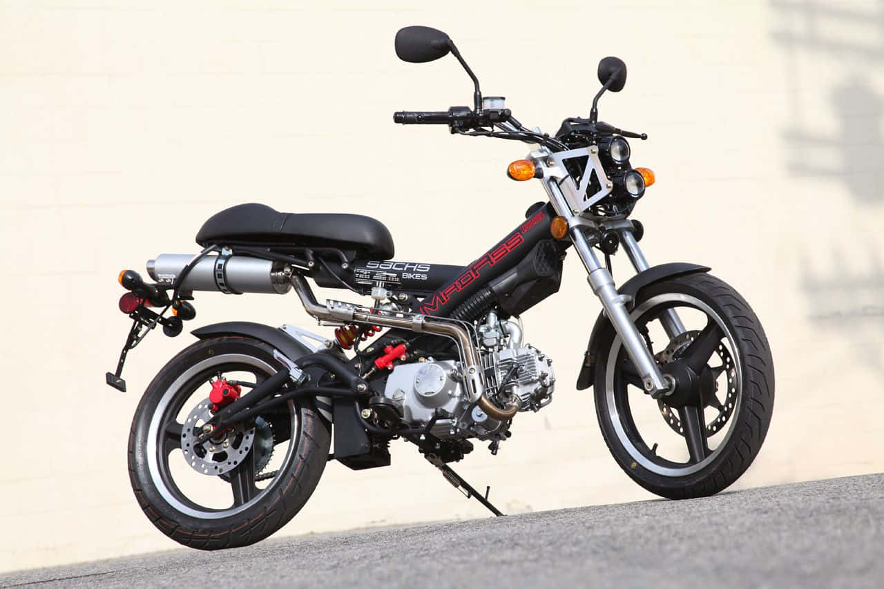 A sleek black and red moped motorcycle with chrome accents stands poised on a paved surface against a plain beige wall., HD Desktop Wallpaper