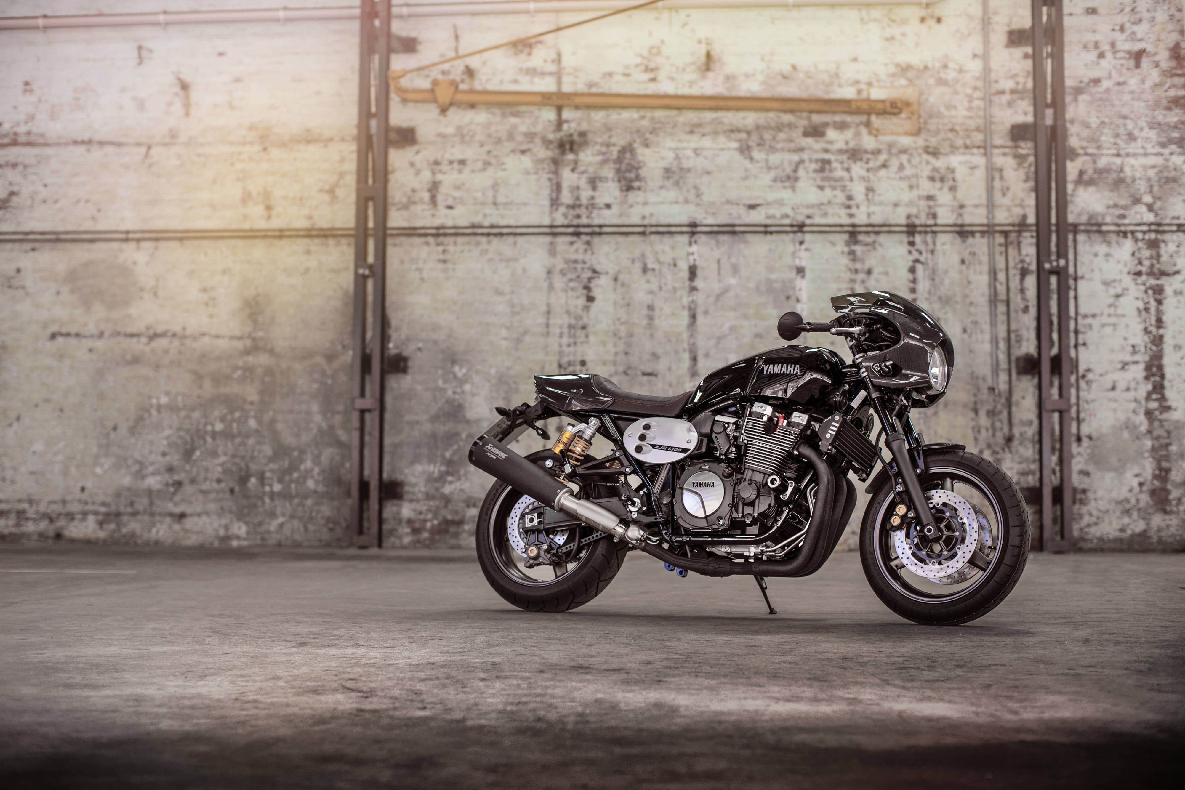 A sleek black Yamaha motorcycle stands poised in a sunlit industrial garage with weathered concrete walls., 4K Desktop Wallpaper