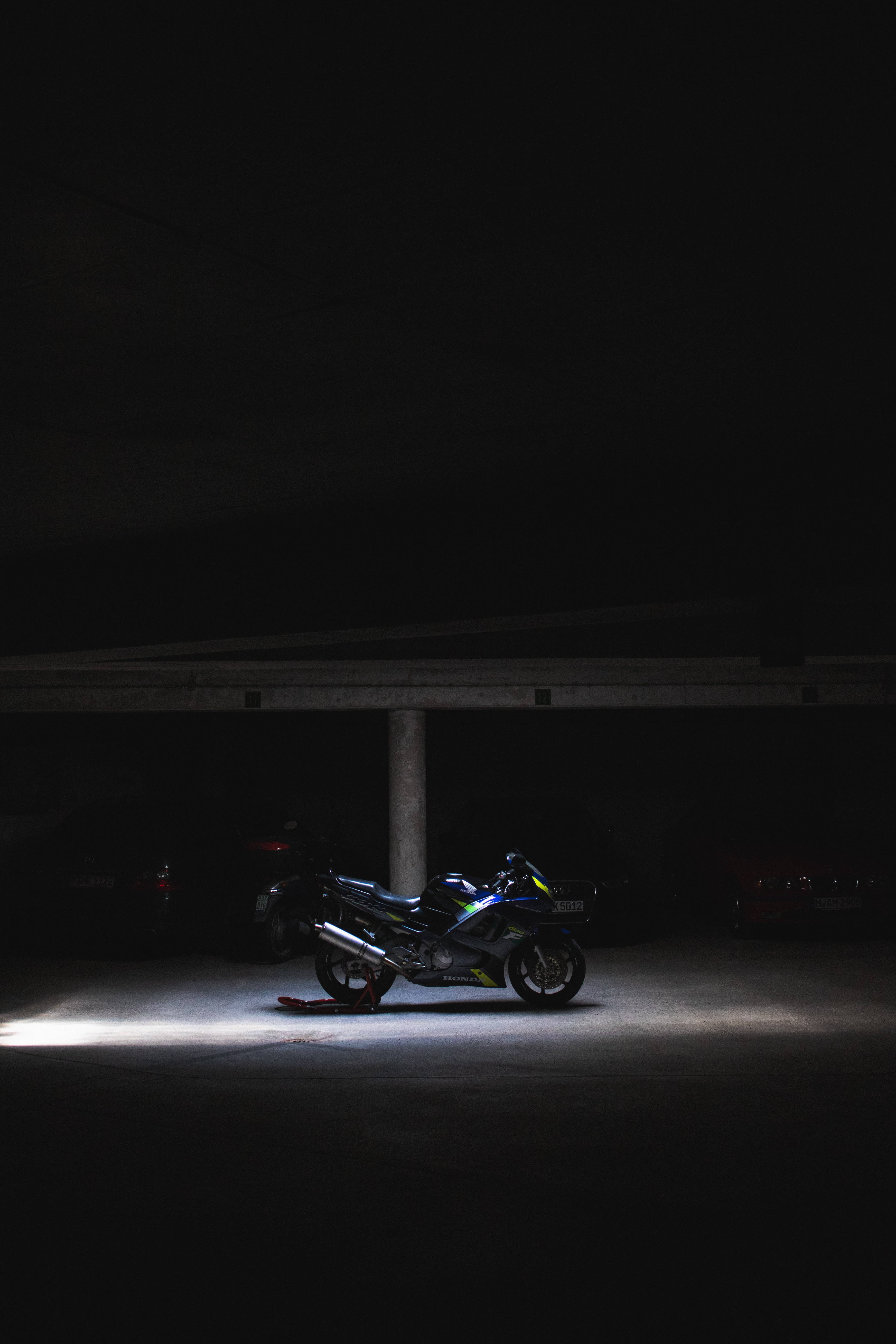 A sleek motorcycle illuminated by a single spotlight in a dark underground parking garage., 5K Phone Wallpaper