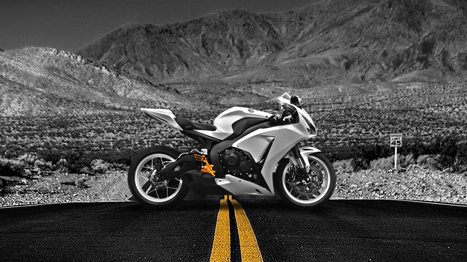 A sleek white sport motorcycle with orange accents stands on a desert road with yellow lines, framed by monochrome mountains and a speed limit sign., Full HD Desktop Wallpaper