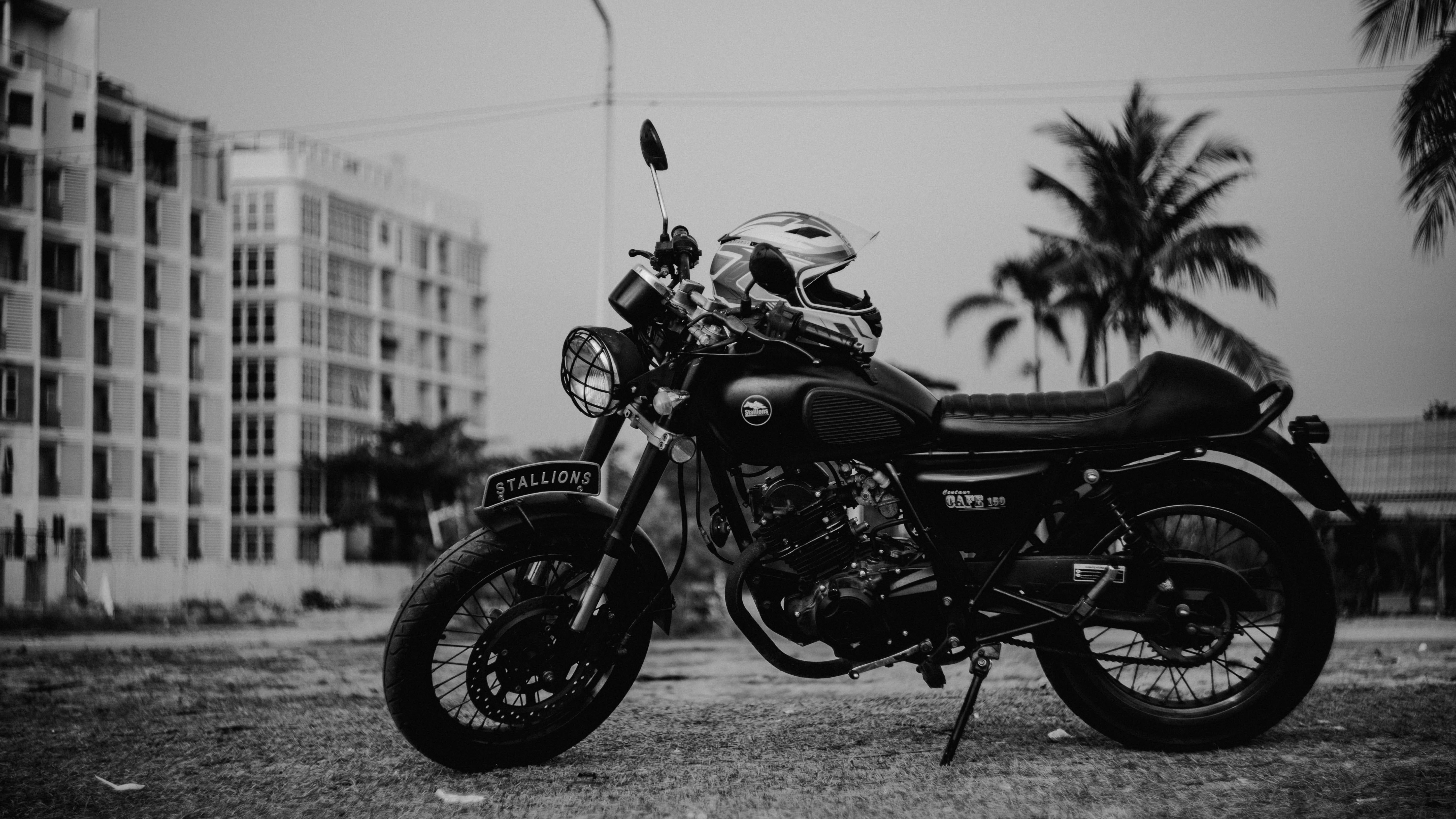 A black motorcycle with a helmet rests on a kickstand in a monochrome urban scene with palm trees and buildings., 5K Desktop Wallpaper