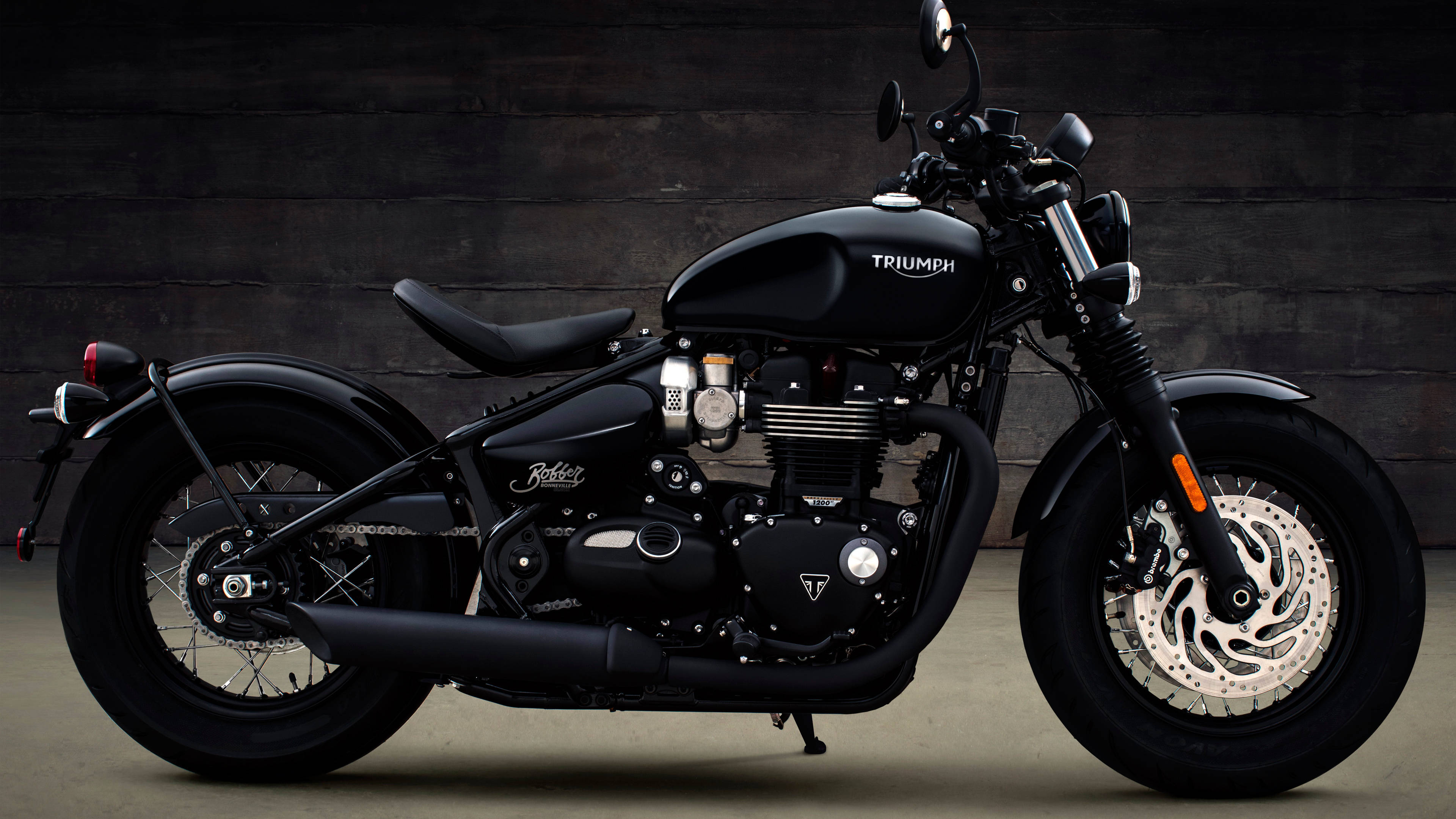 A sleek black Triumph motorcycle stands poised against a dark wooden wall in a studio setting., 4K Desktop Wallpaper