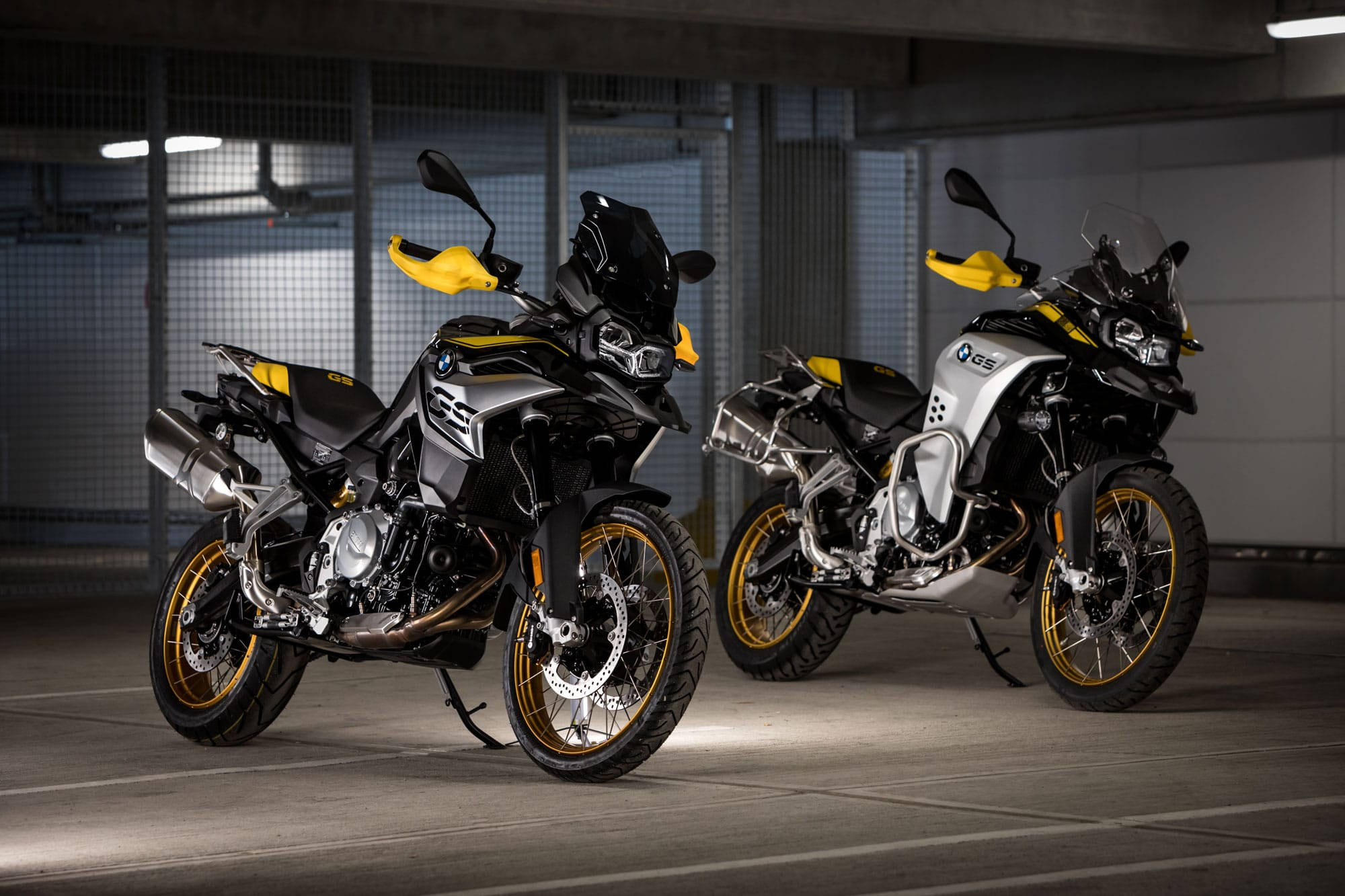 Two sleek BMW GS adventure motorcycles with bold yellow accents stand poised in a dimly lit underground parking garage., Full HD Desktop Wallpaper