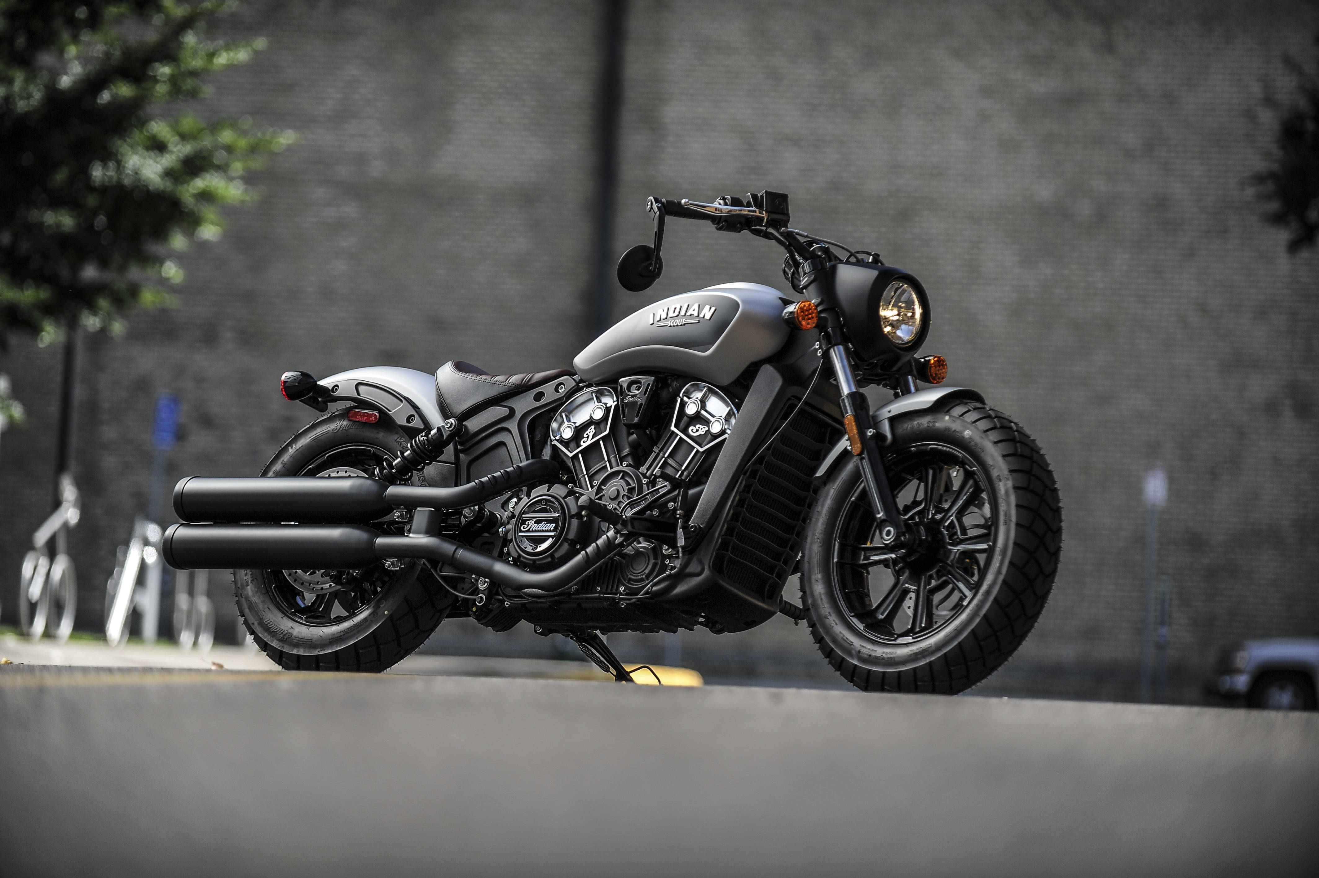 A matte gray Indian motorcycle with black accents stands parked on a city street against a brick wall., 4K Desktop Wallpaper