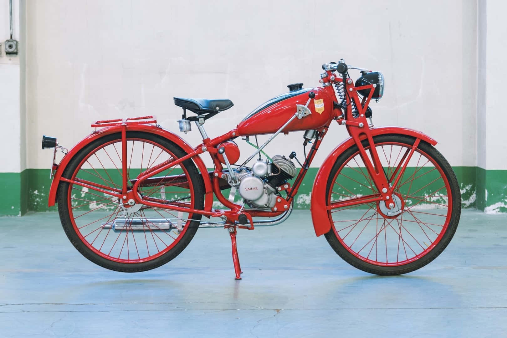 A vintage red motorcycle with chrome accents stands on a kickstand in a minimalist garage with green and white walls., HD Desktop Wallpaper