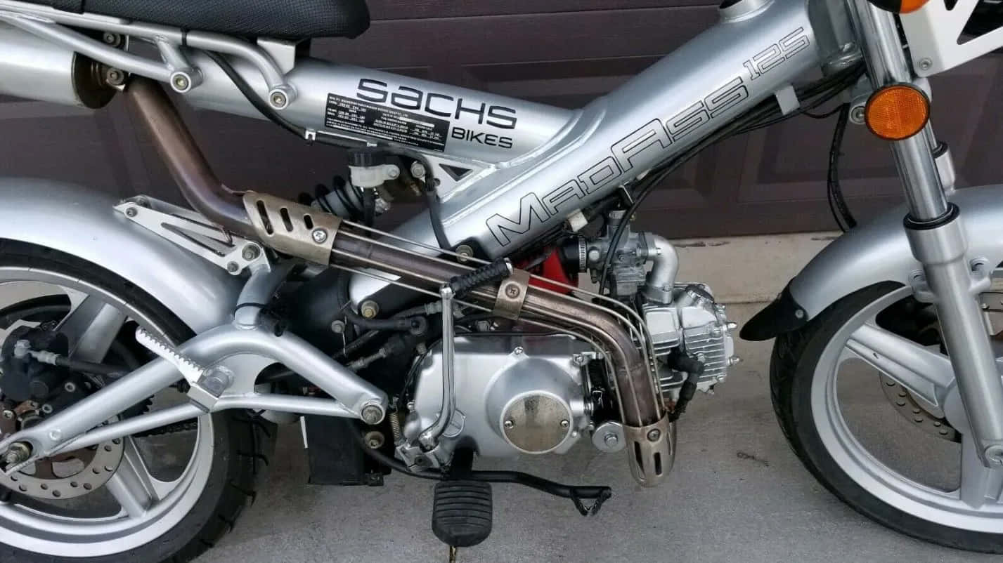 Close-up of a silver Sachs Madass 125 motorcycle showcasing its engine and mechanical details against a garage door., HD Desktop Wallpaper