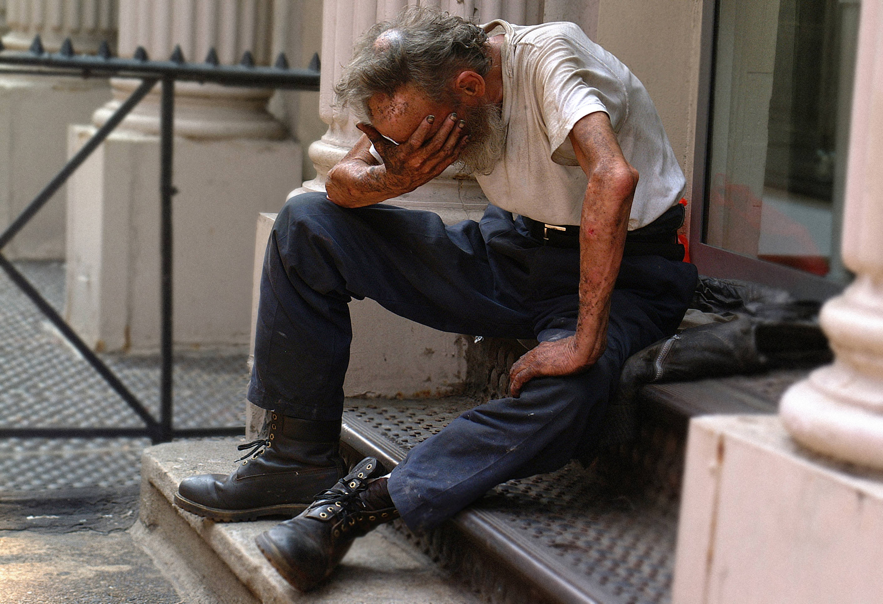 An elderly man with a grizzled beard sits slumped on urban steps, head in hands, wearing a stained shirt and boots., 2K Desktop Wallpaper
