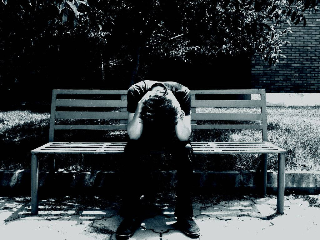 A person sits hunched on a park bench with head buried in hands in stark black and white., SD Desktop Wallpaper