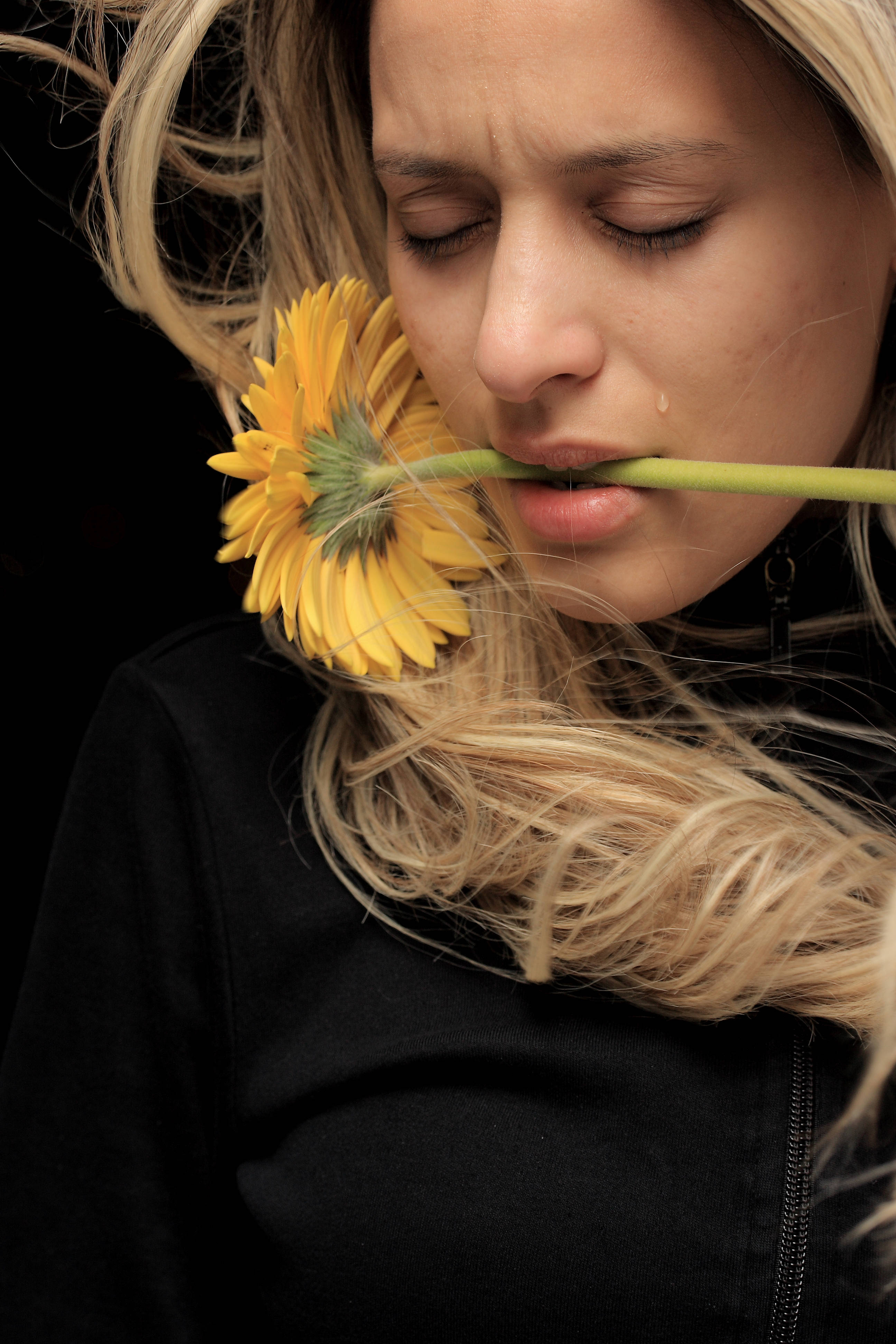 A woman with closed eyes and a tear holds a yellow gerbera daisy to her lips against a black background., 4K Phone Wallpaper