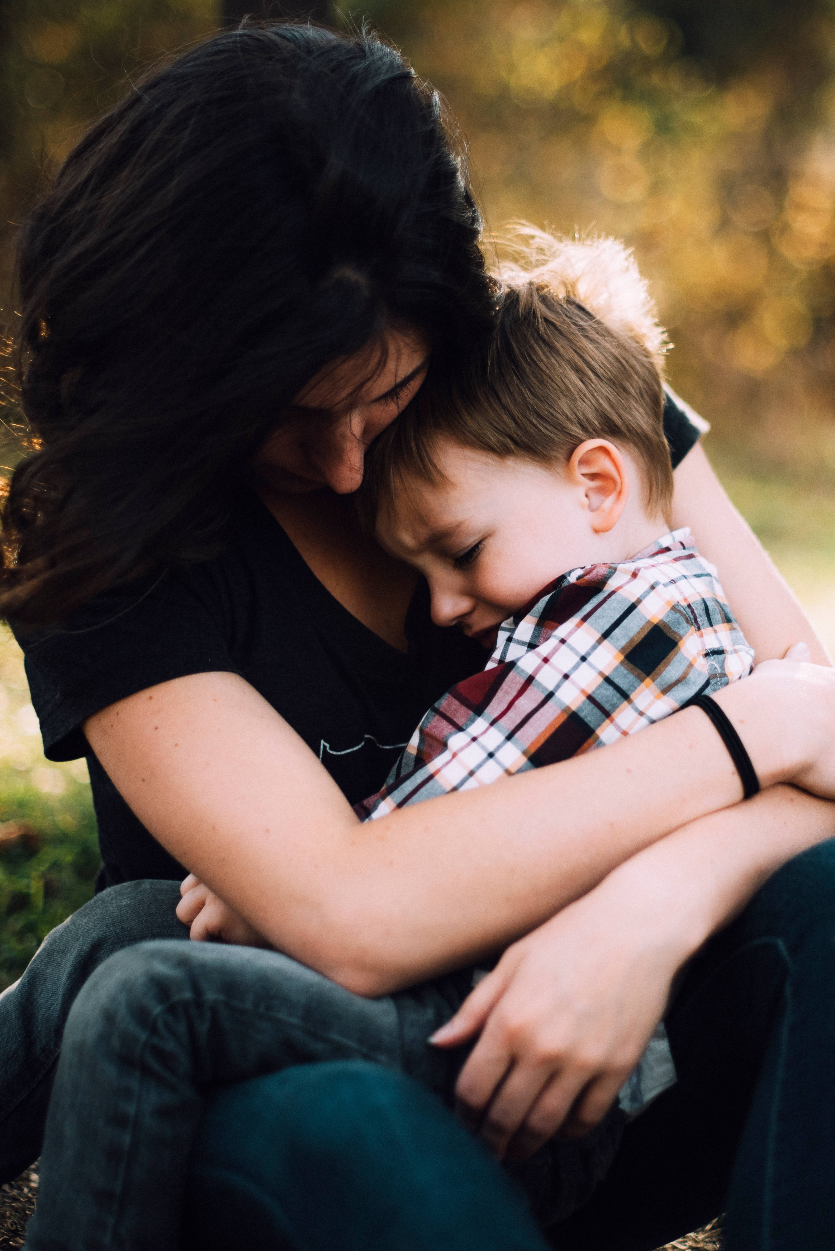 A mother tenderly embraces her young son in a sunlit outdoor setting with golden bokeh background., 4K Phone Wallpaper