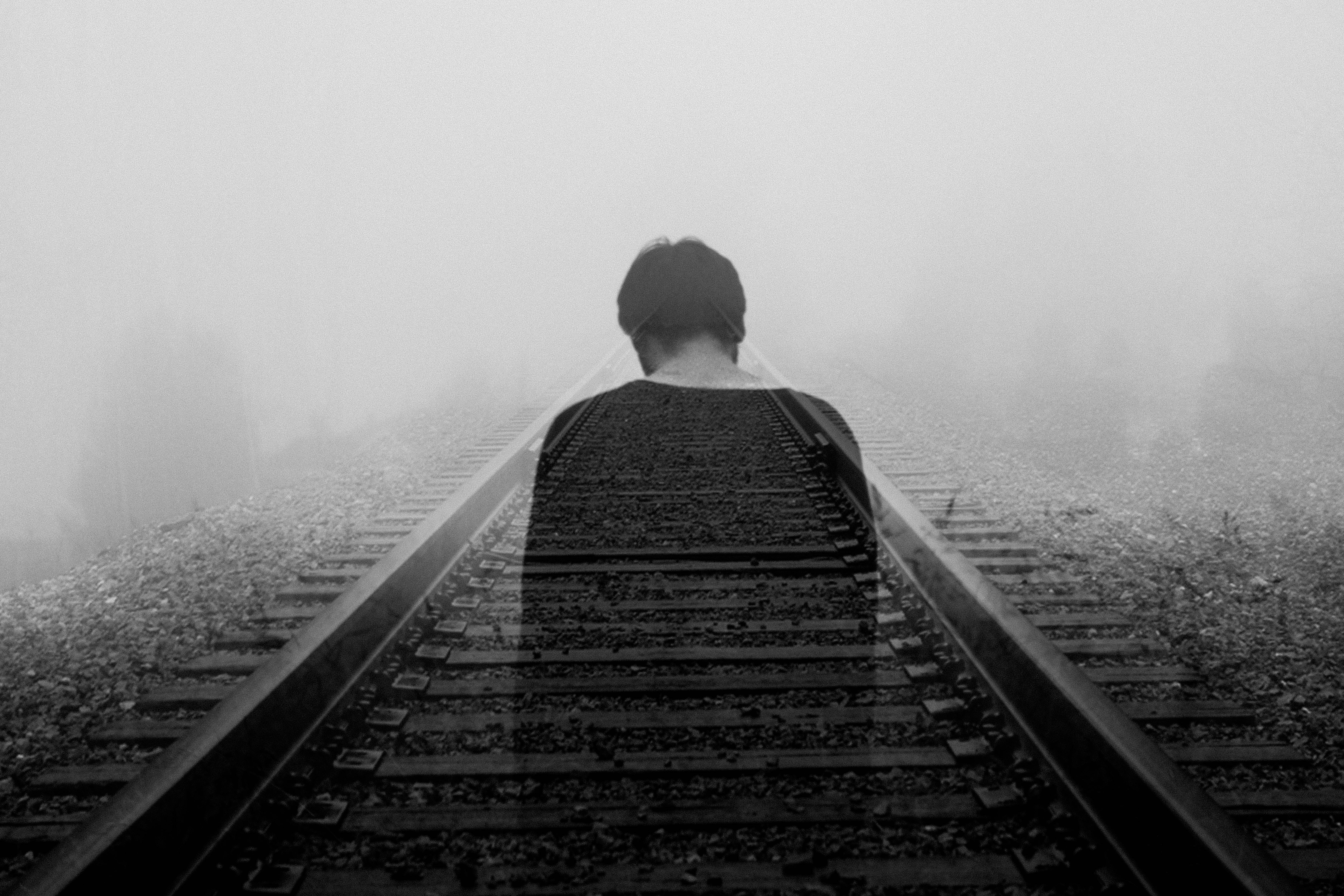 A lone figure walks away down a foggy railway track in monochrome, creating a mysterious and contemplative atmosphere., 5K Desktop Wallpaper