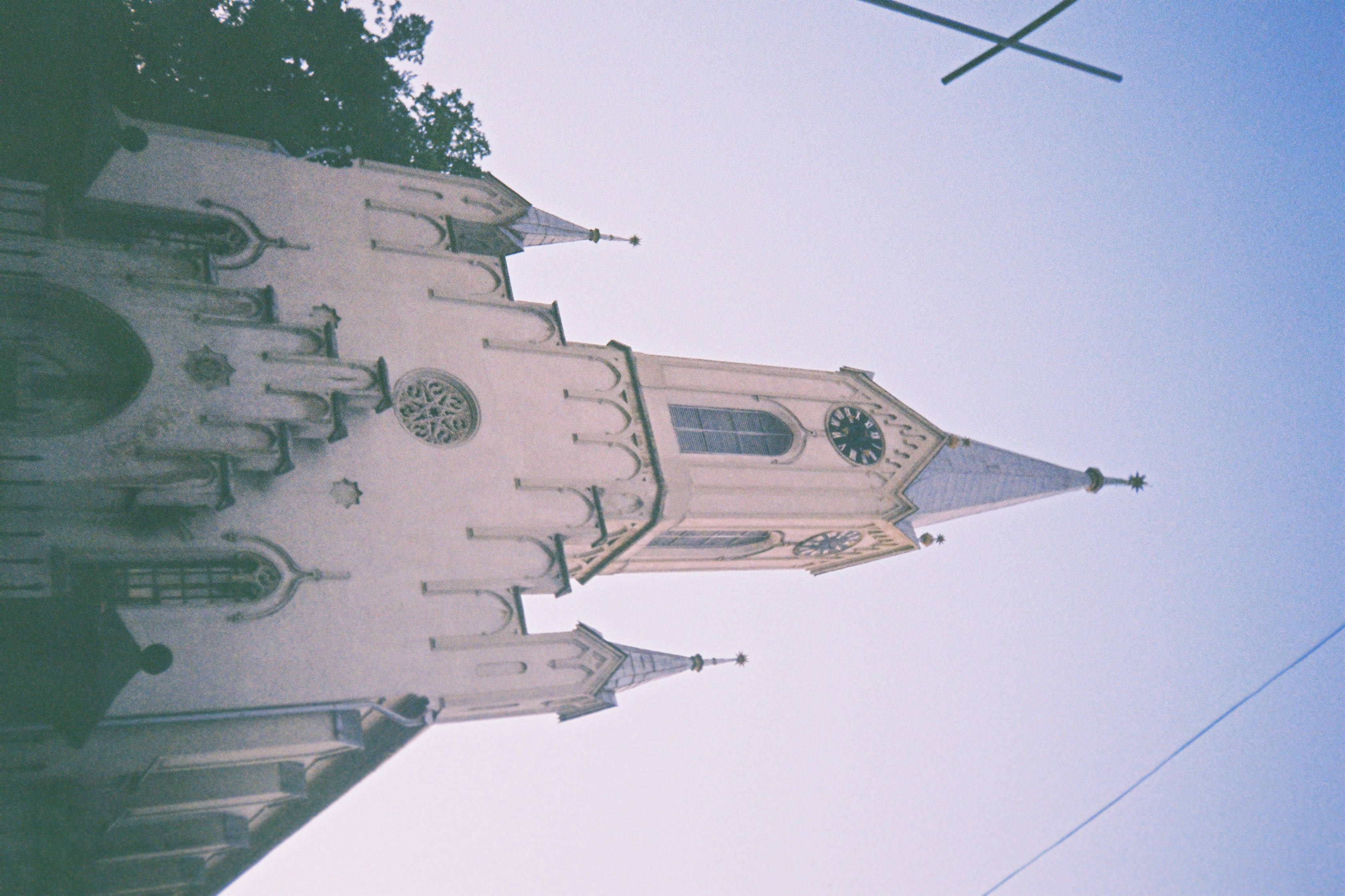 A low-angle view of a white Gothic church with pointed spires and a clock tower against a pale blue sky., 2K Desktop Wallpaper