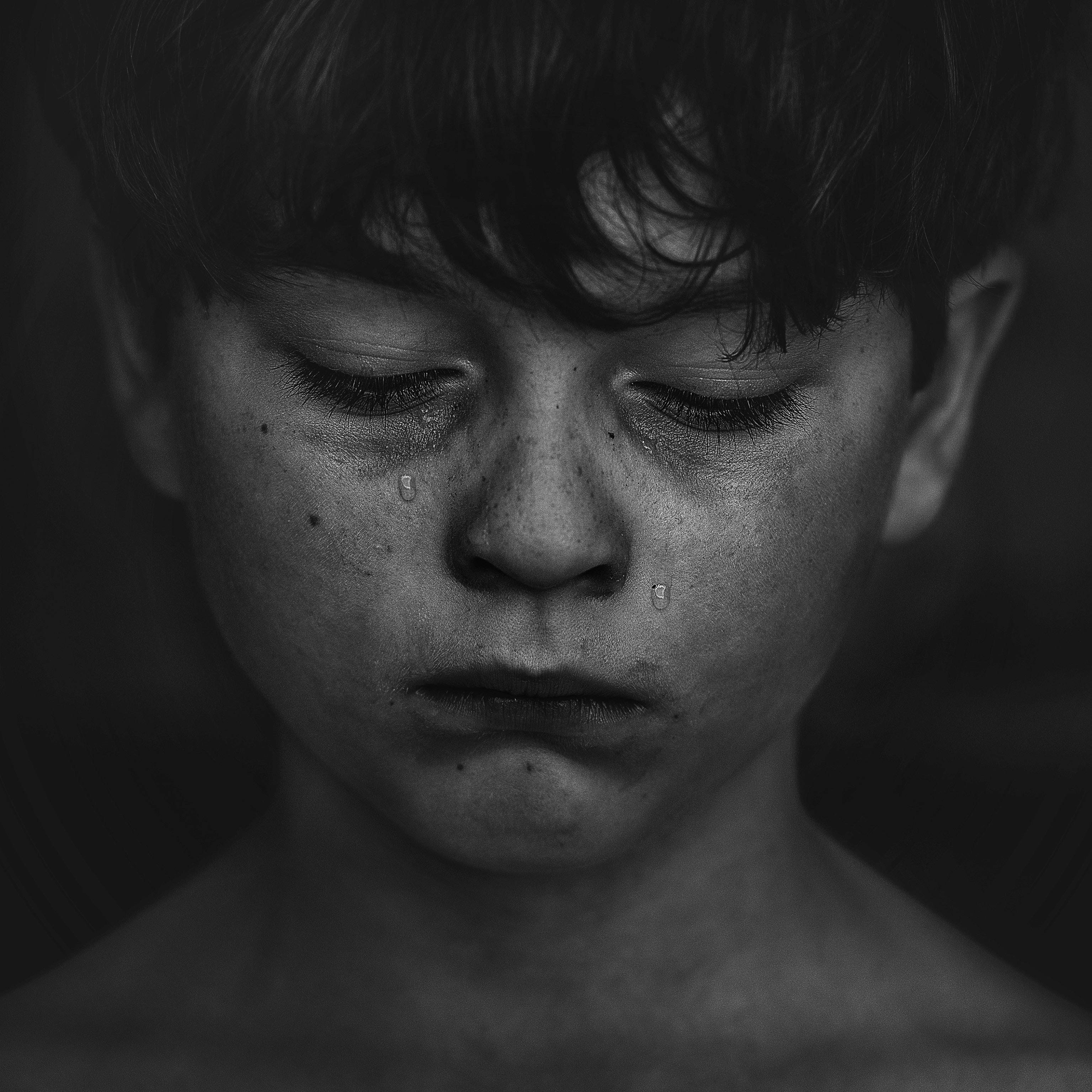 A black and white close-up of a young boy's face with tears streaming down his cheeks in a poignant moment of sorrow., 2K Desktop Wallpaper