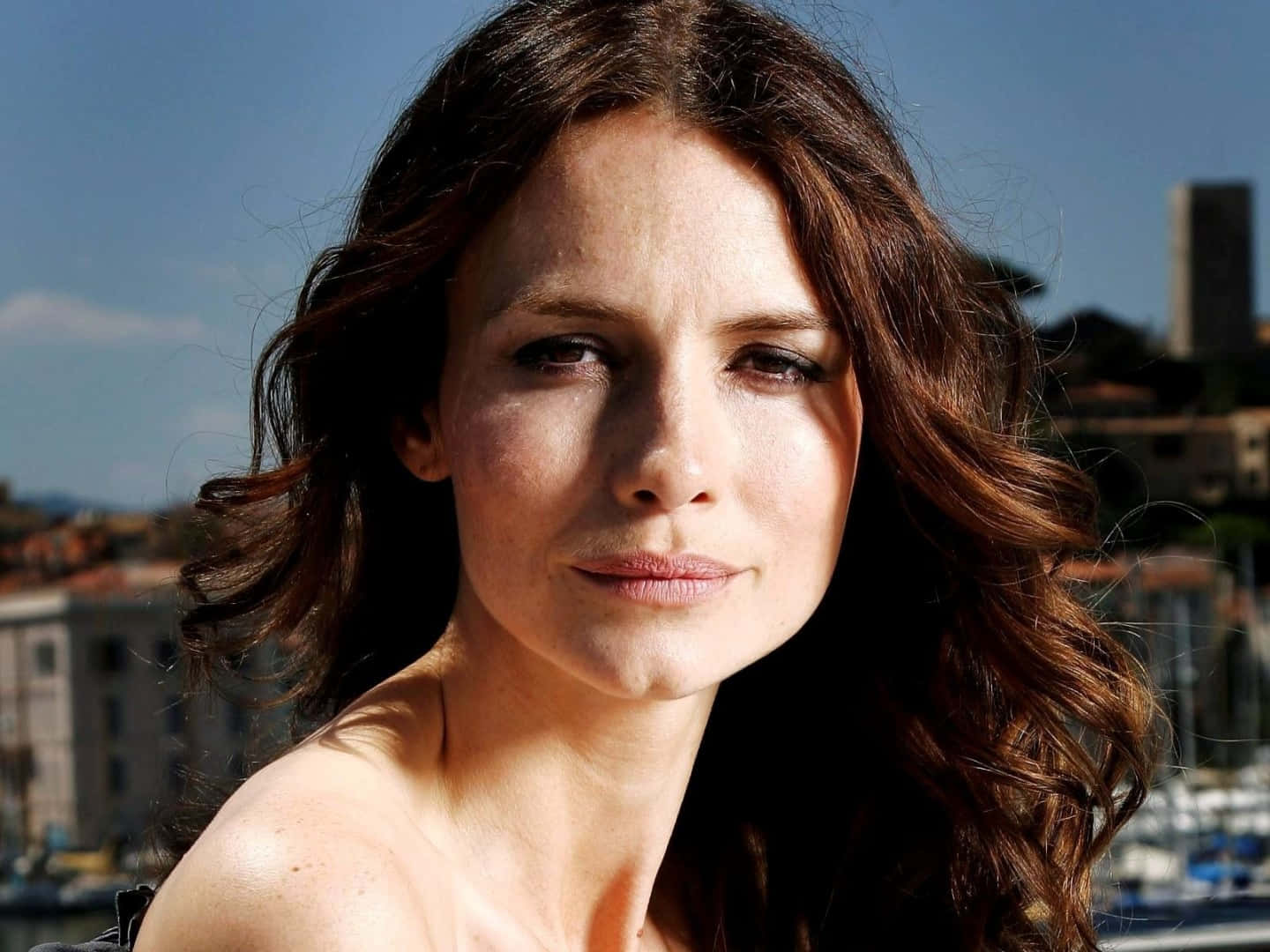 Saffron Burrows, wavy brown hair, sunlit coastal city, HD Desktop Wallpaper