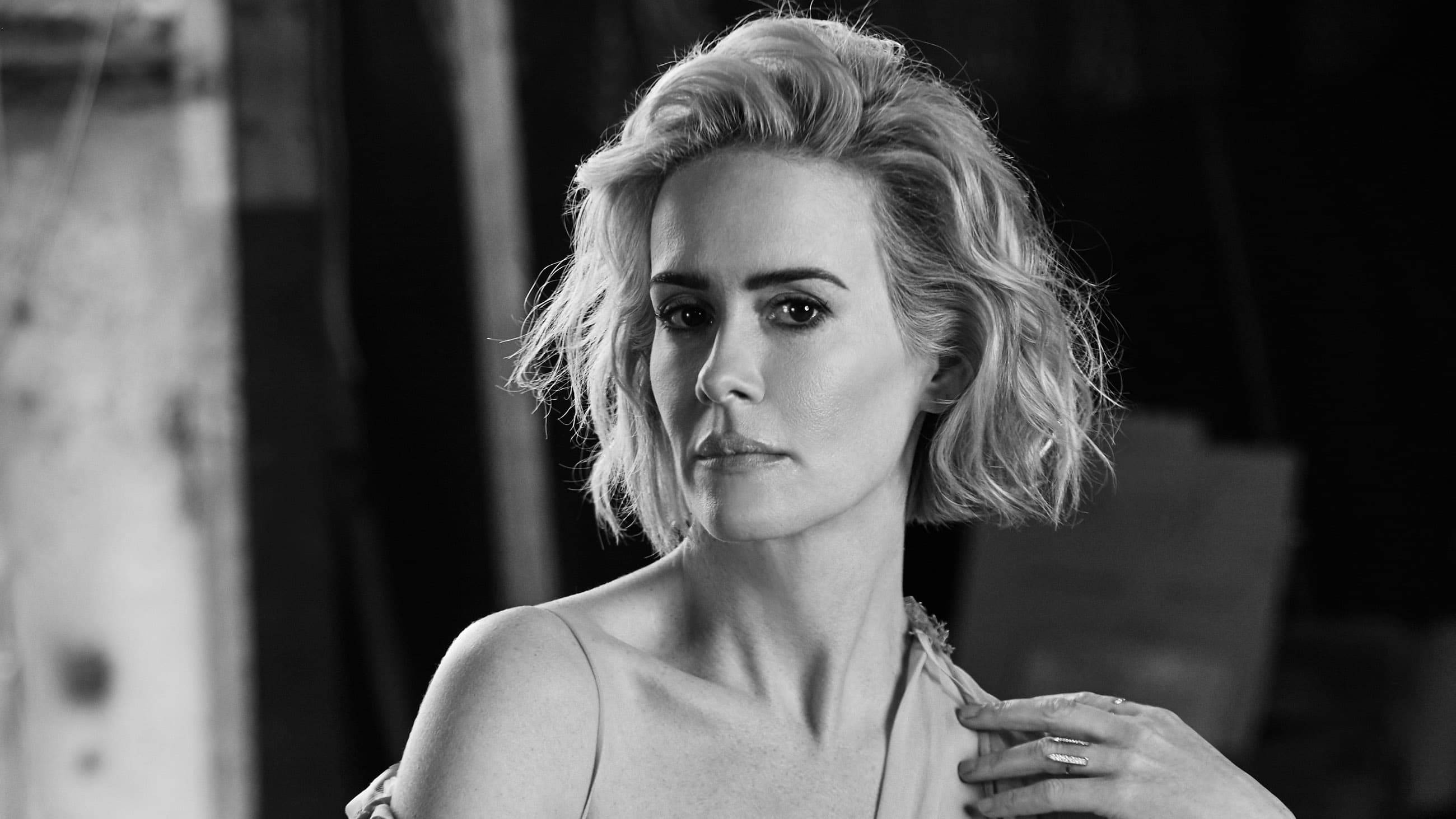 Sarah Paulson, tousled blonde hair, dimly lit industrial setting, 2K Desktop Wallpaper