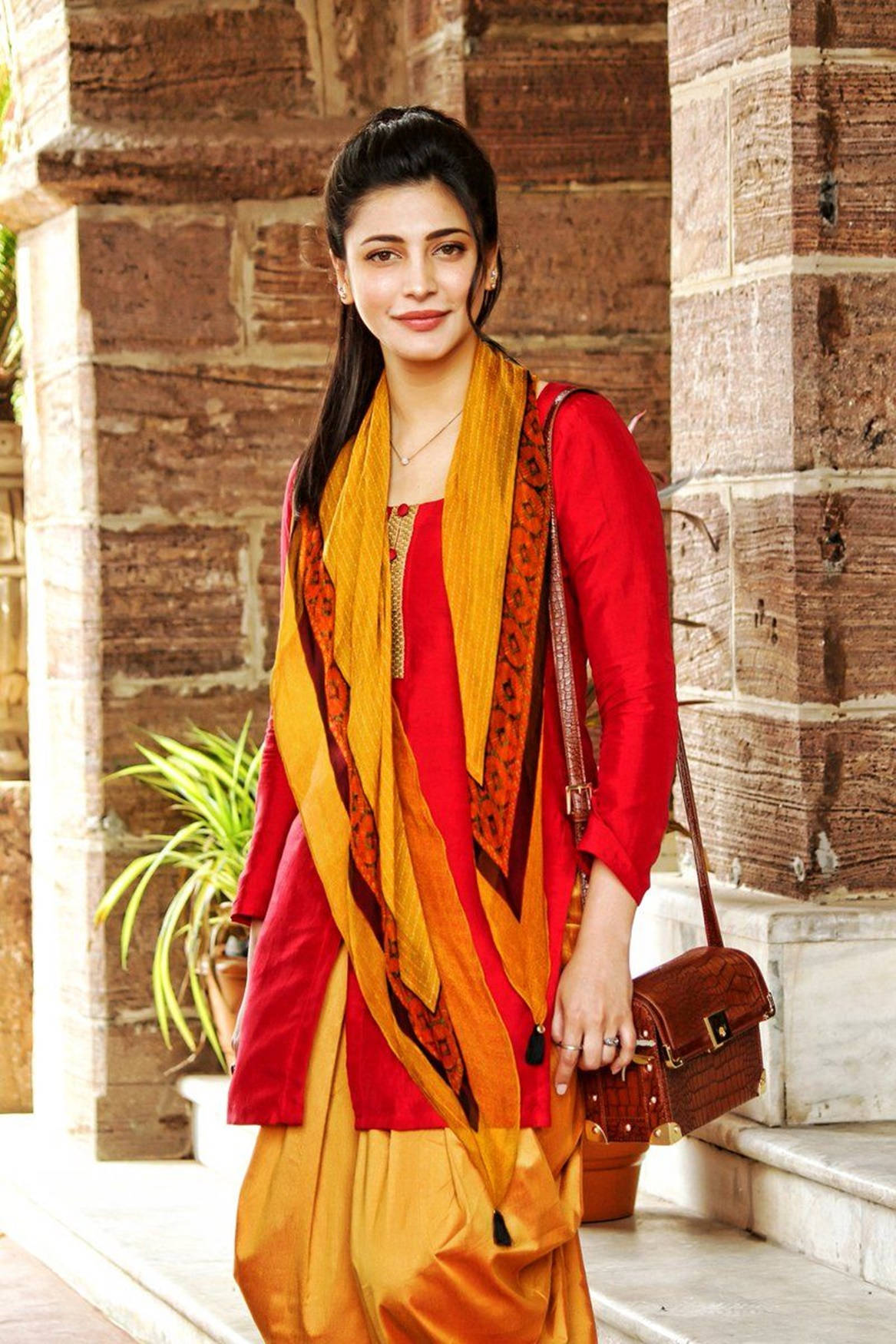 Shruti Hassan, vibrant red and orange traditional attire, rustic brick wall, HD Phone Wallpaper