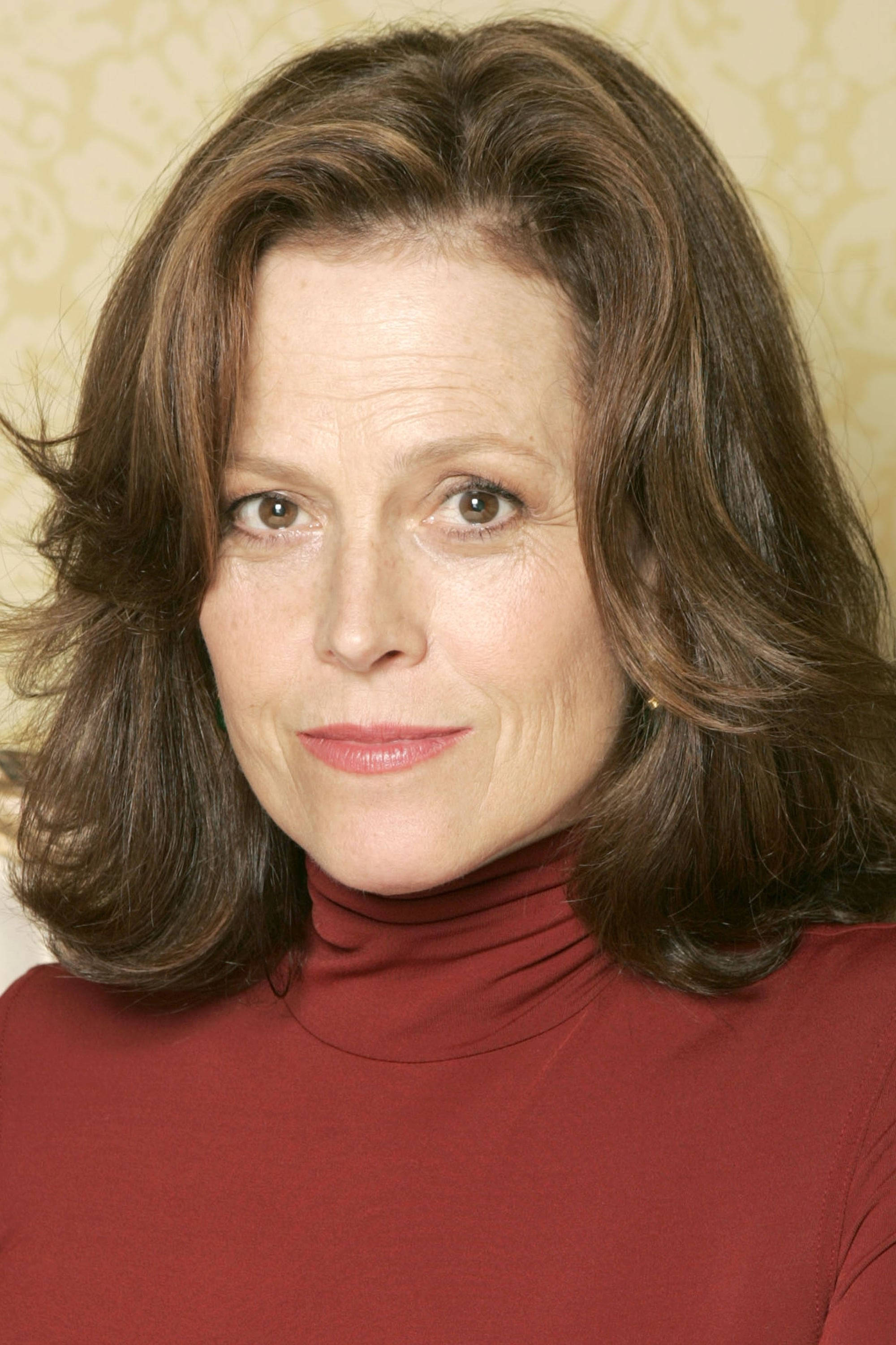 Sigourney Weaver, red turtleneck, beige wall, 2K Phone Wallpaper