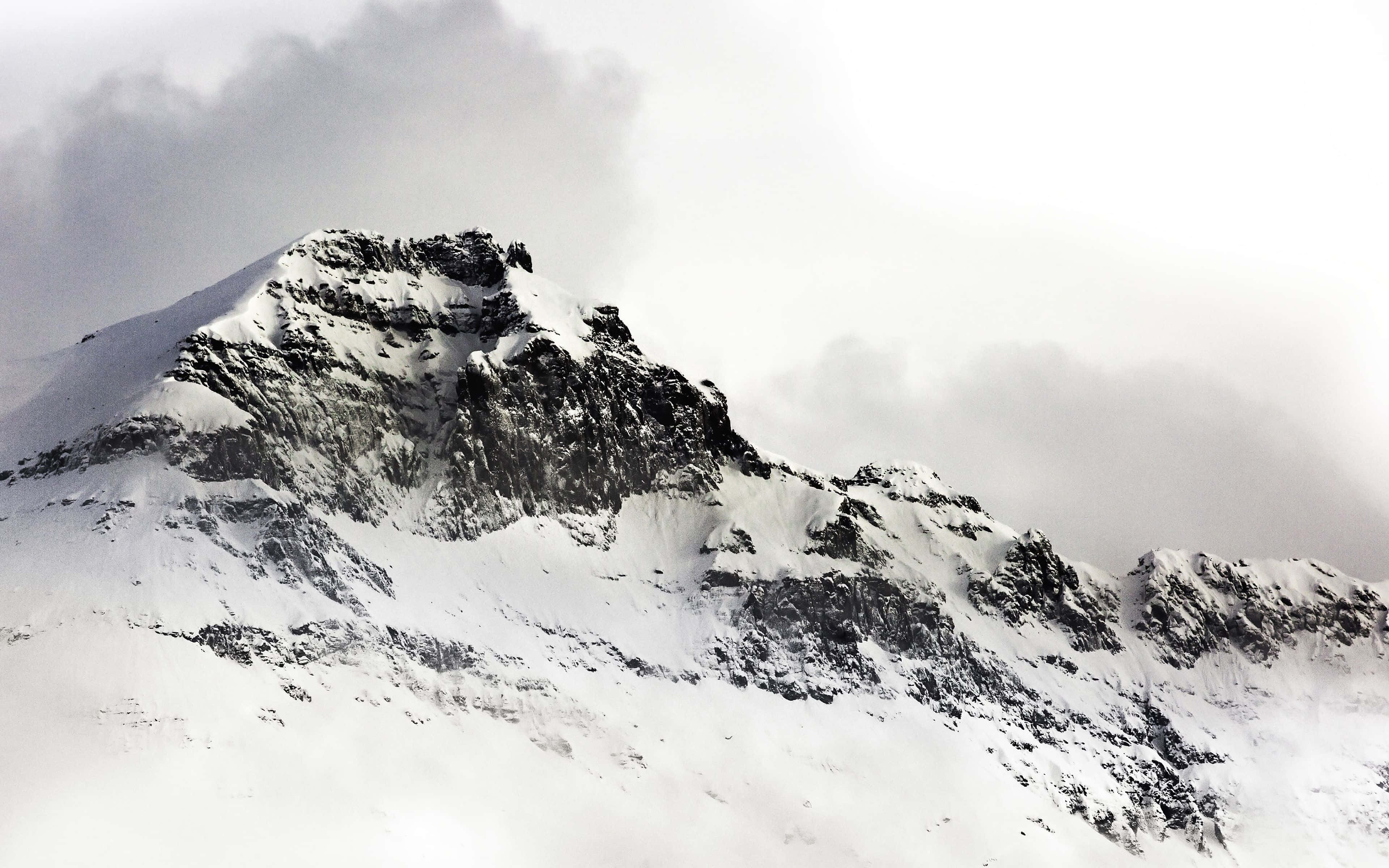 snow-covered mountain, dark rocky outcrops, cloudy gray sky, 4K Desktop Wallpaper