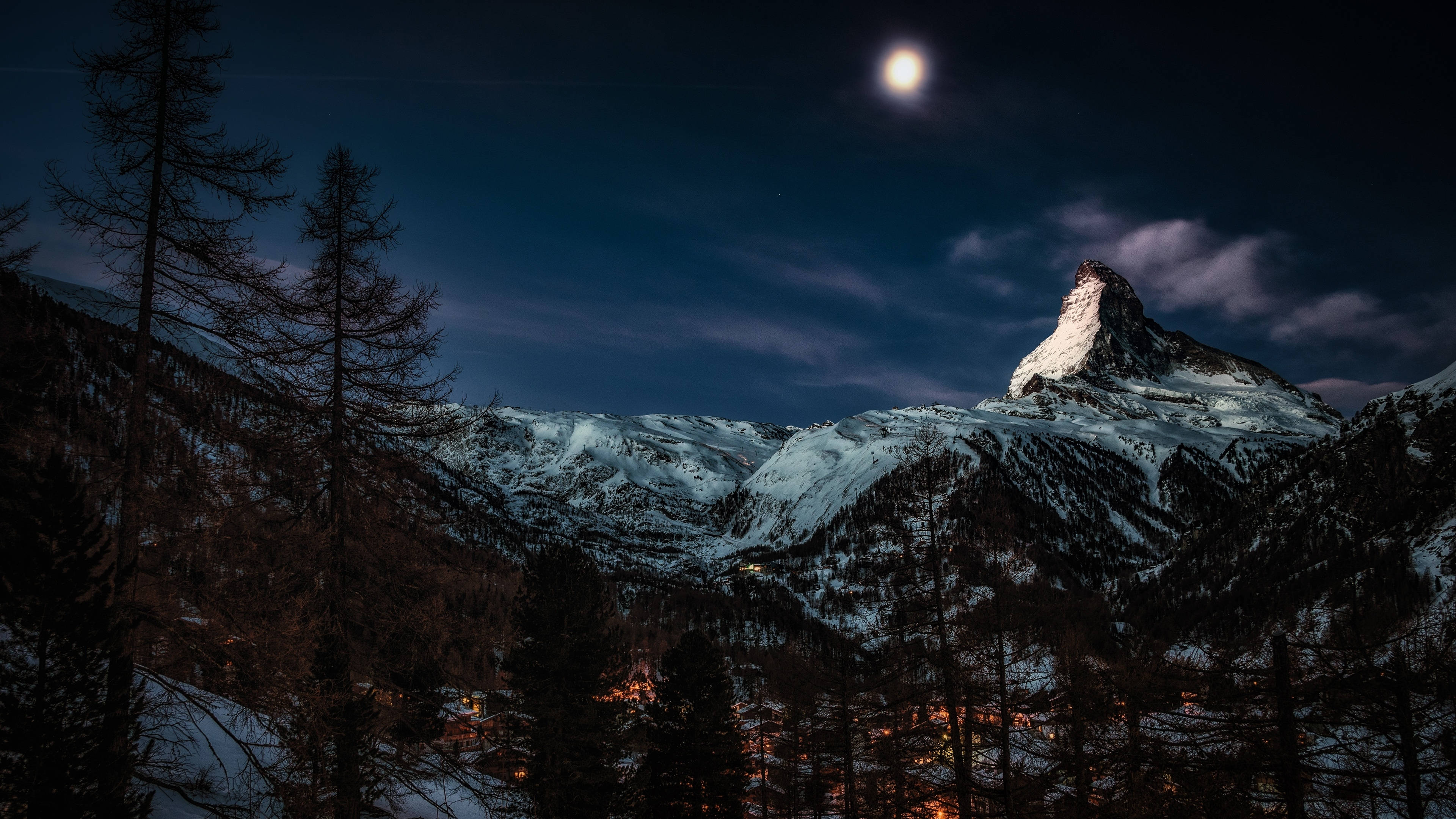 Moonlit snow-capped mountain peak, forested valley, glowing village lights, 4K Desktop Wallpaper