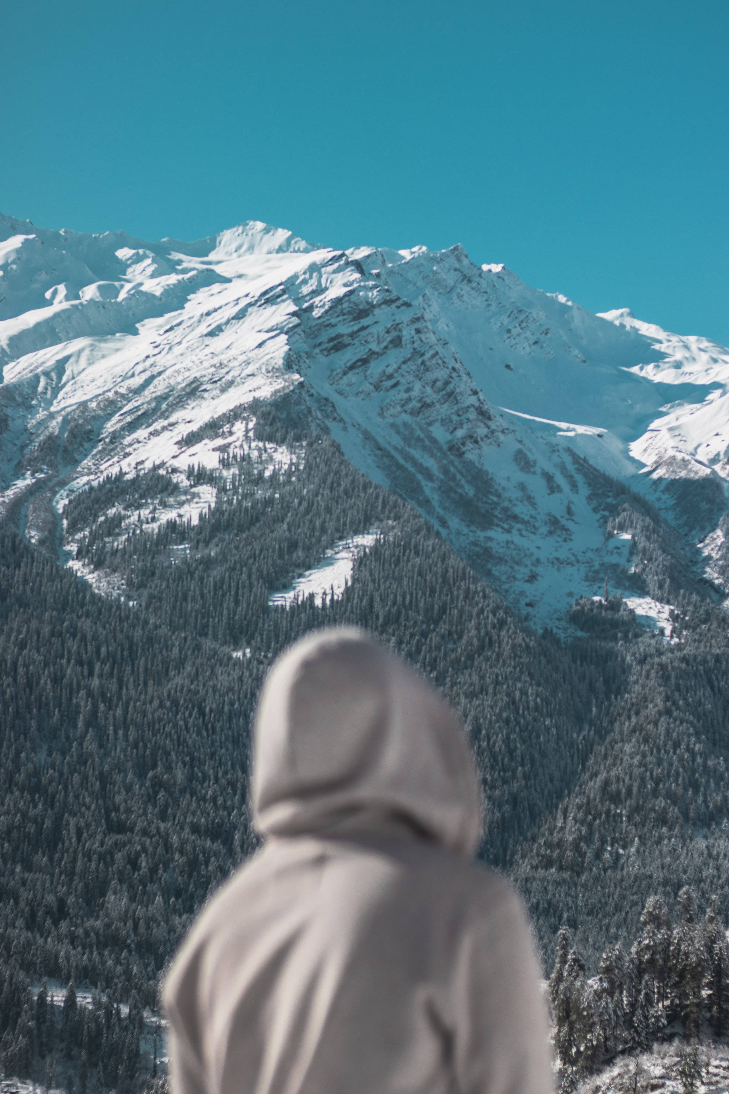 hooded figure, snow-capped mountains, clear blue sky, 2K Phone Wallpaper