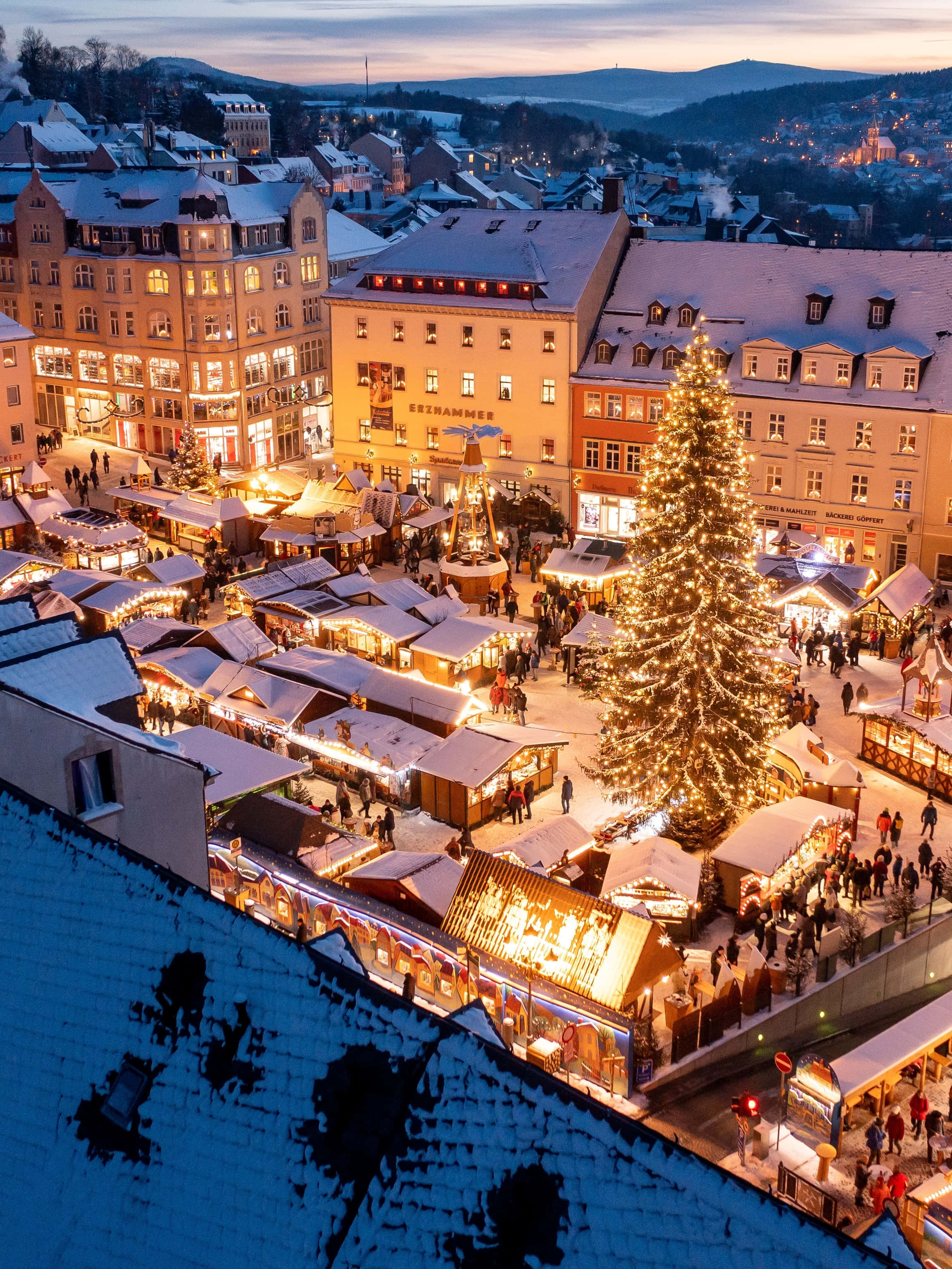 snowy European town square, dusk, glowing Christmas tree, 2K Phone Wallpaper
