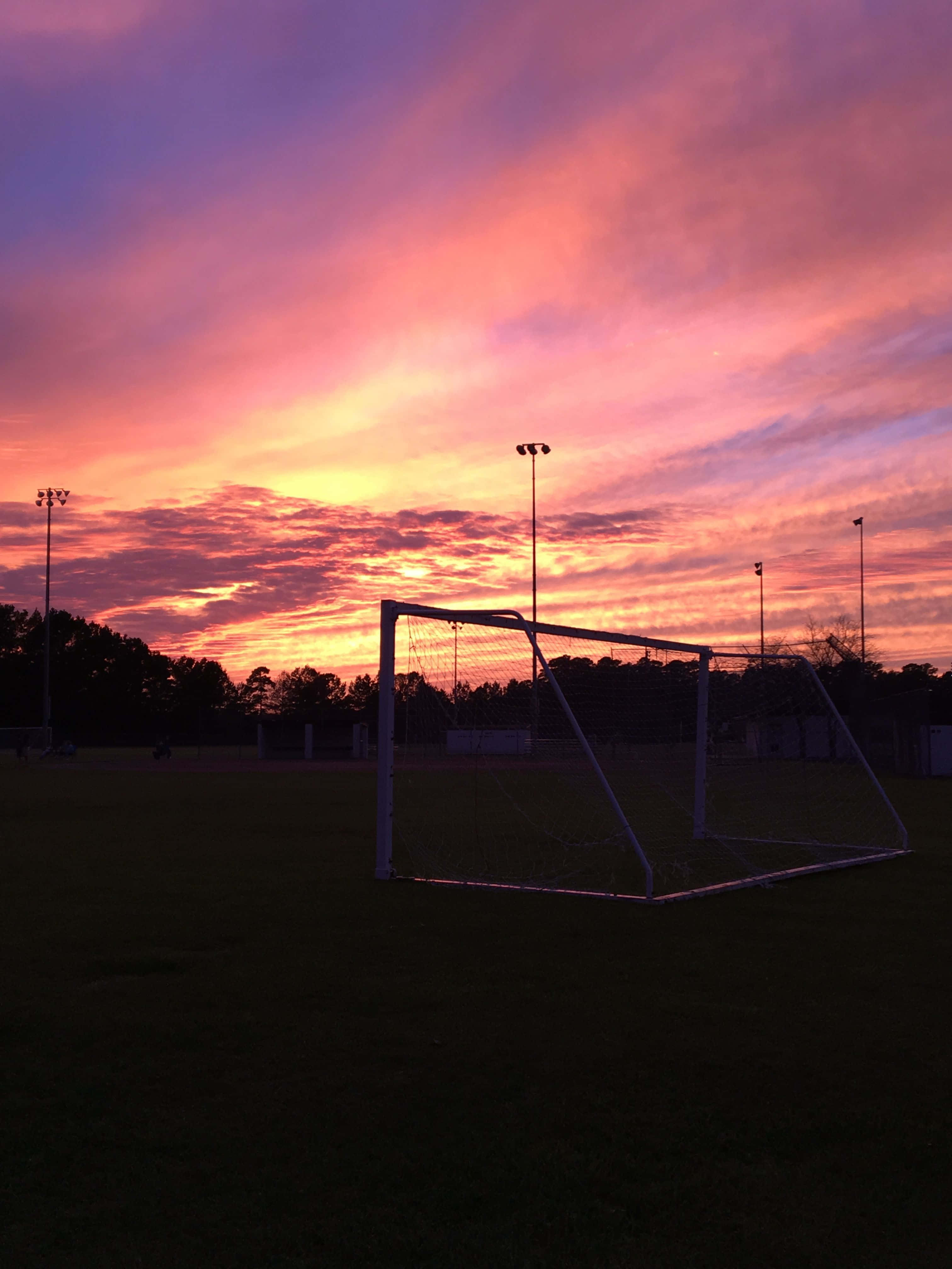 soccer goal, vibrant sunset sky, fiery orange pink and purple clouds, 4K Phone Wallpaper