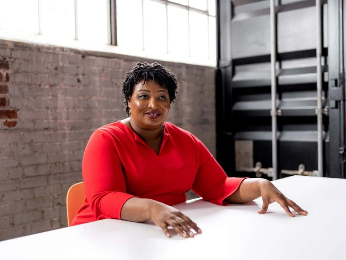 Stacey Abrams, vibrant red top, white table, SD Desktop Wallpaper