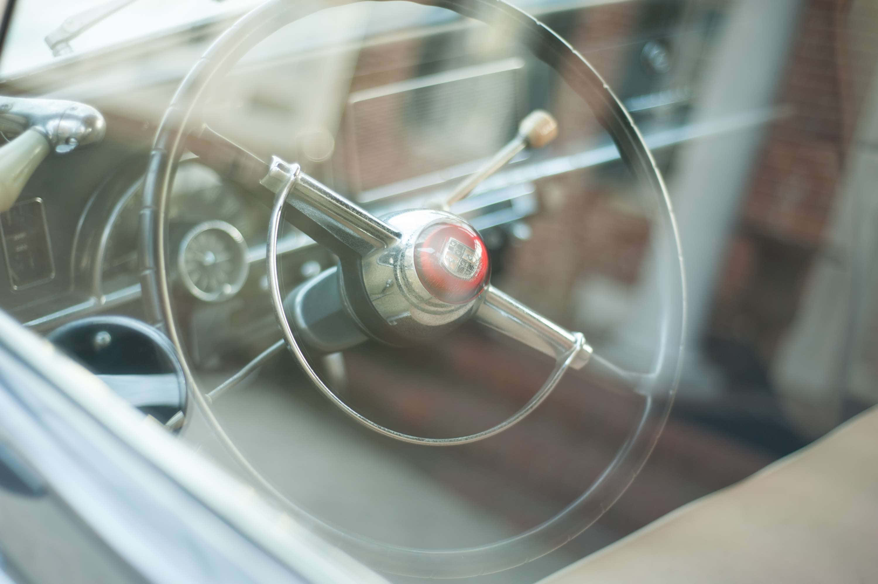 chrome steering wheel, red center emblem, sunlit windshield, 2K Desktop Wallpaper
